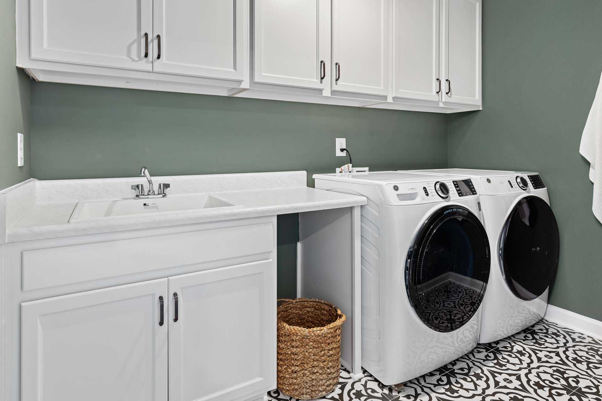 Modern laundry room in Sierra Heights, Clayton NC with white washer dryer, utility sink, cabinets, and sage green walls