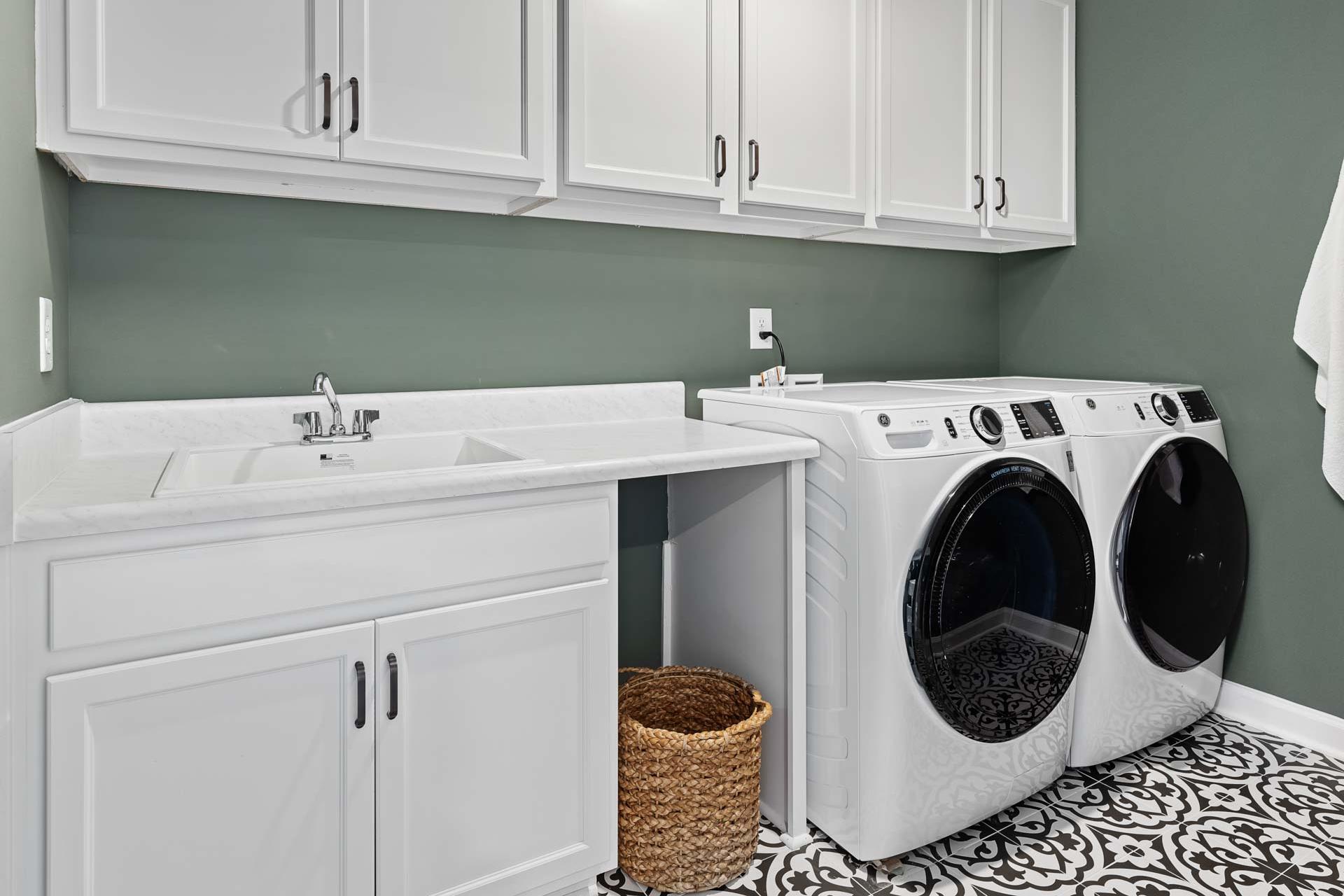 Modern laundry room in Sierra Heights, Clayton NC with white washer dryer, utility sink, cabinets, and sage green walls