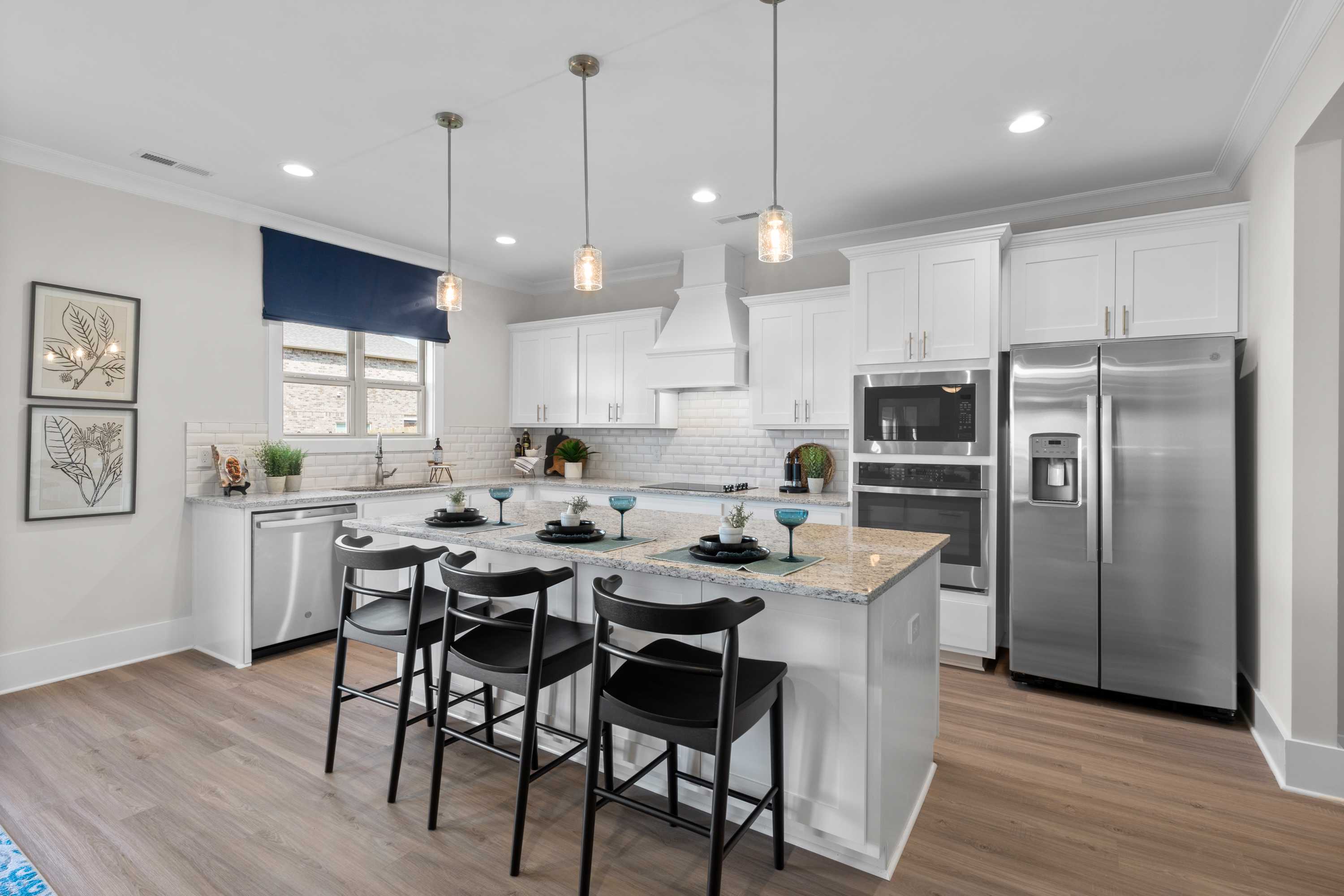 Spacious kitchen in The Chelsea B featuring white shaker cabinets, large granite island with black stools, stainless steel appliances