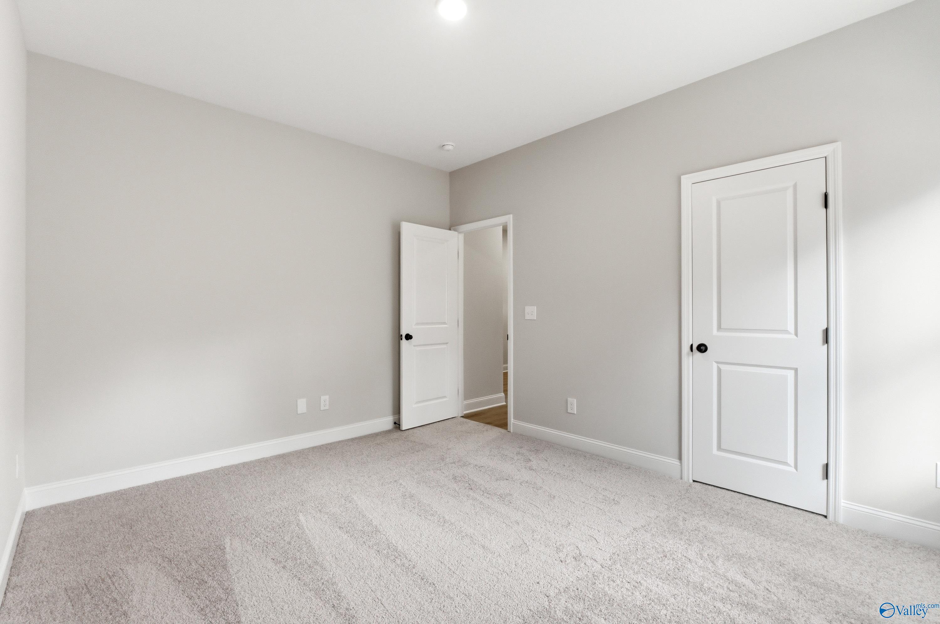 Bright secondary bedroom with light gray walls, neutral carpet, and adjacent door in Davidson Homes The Daphne C, Huntsville, Alabama