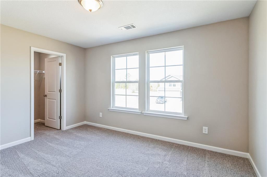 Bright secondary bedroom with beige walls, carpet flooring, double windows, and closet in Evermore Homes The Stella, Perry, Georgia