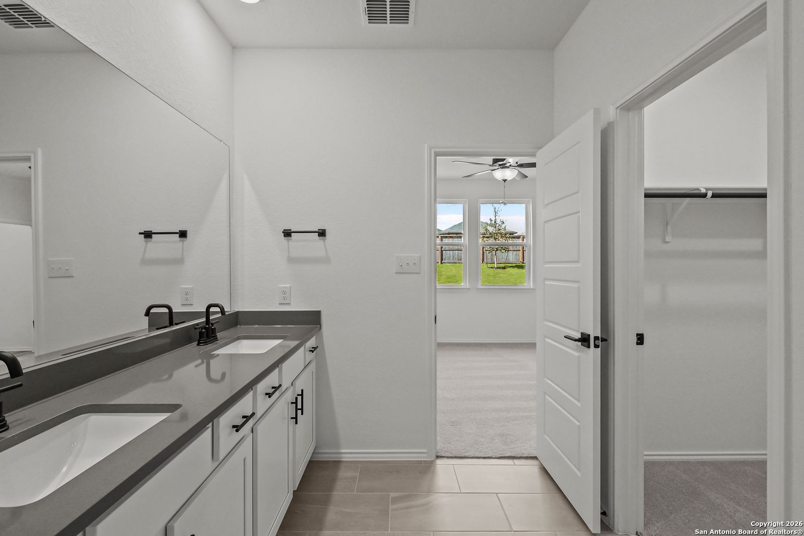 Modern master bathroom with dual sinks, white quartz vanity, large mirror, and walk-in closet in Davidson Homes The Douglas E, San Antonio