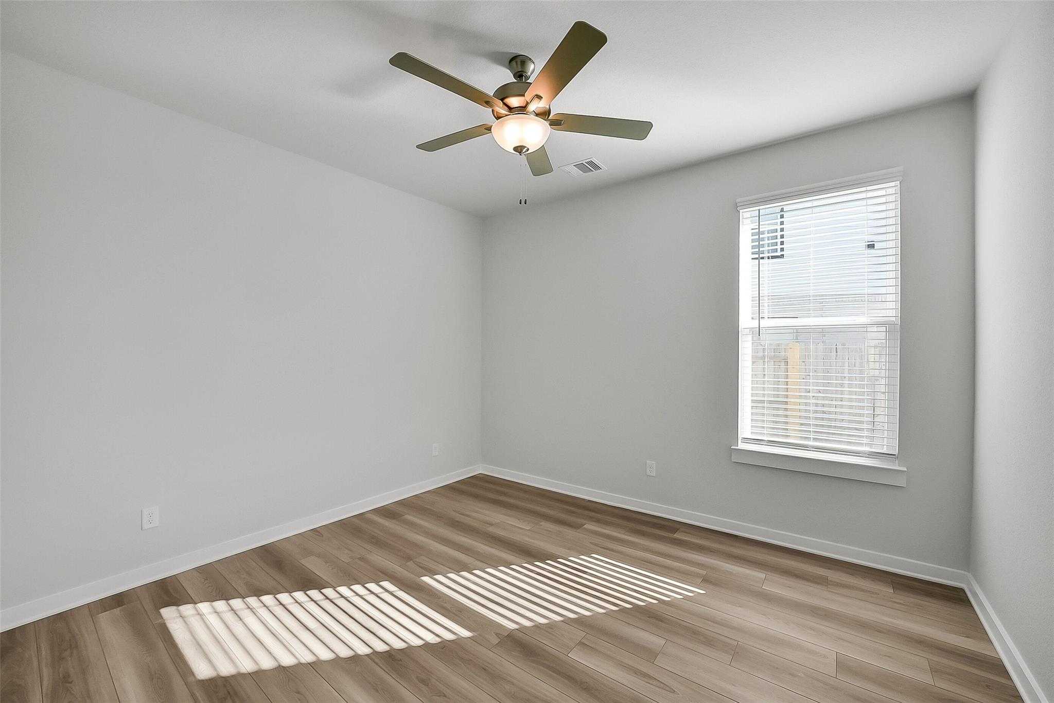 Bright secondary bedroom with ceiling fan, blinds window, and luxury vinyl plank floors in Davidson Homes The Acadia A, Sunterra, Katy, Texas