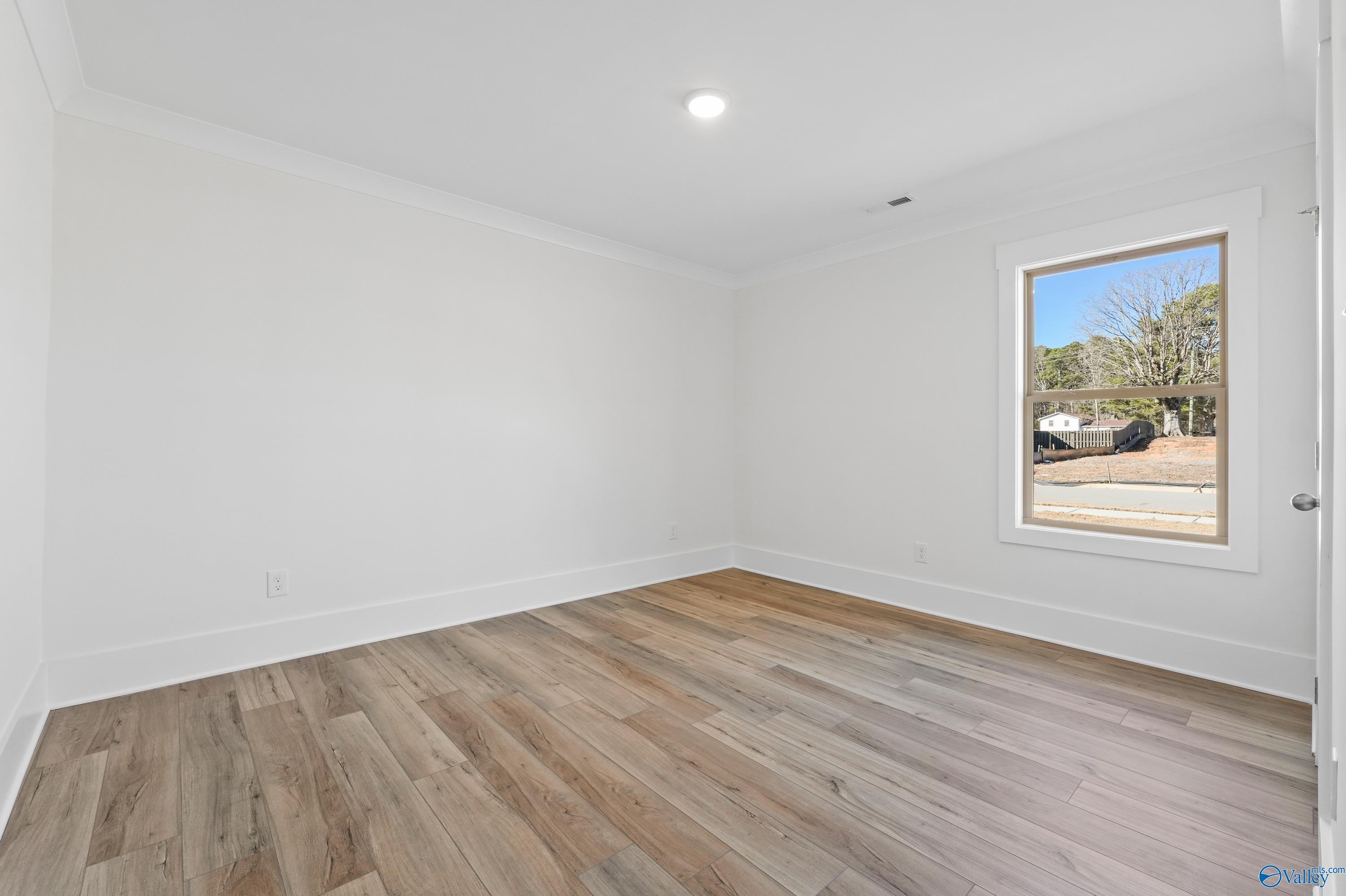 Bright empty bedroom featuring hardwood floors and large window in The Daphne C 4-bedroom home by Davidson Homes, Arab, Alabama