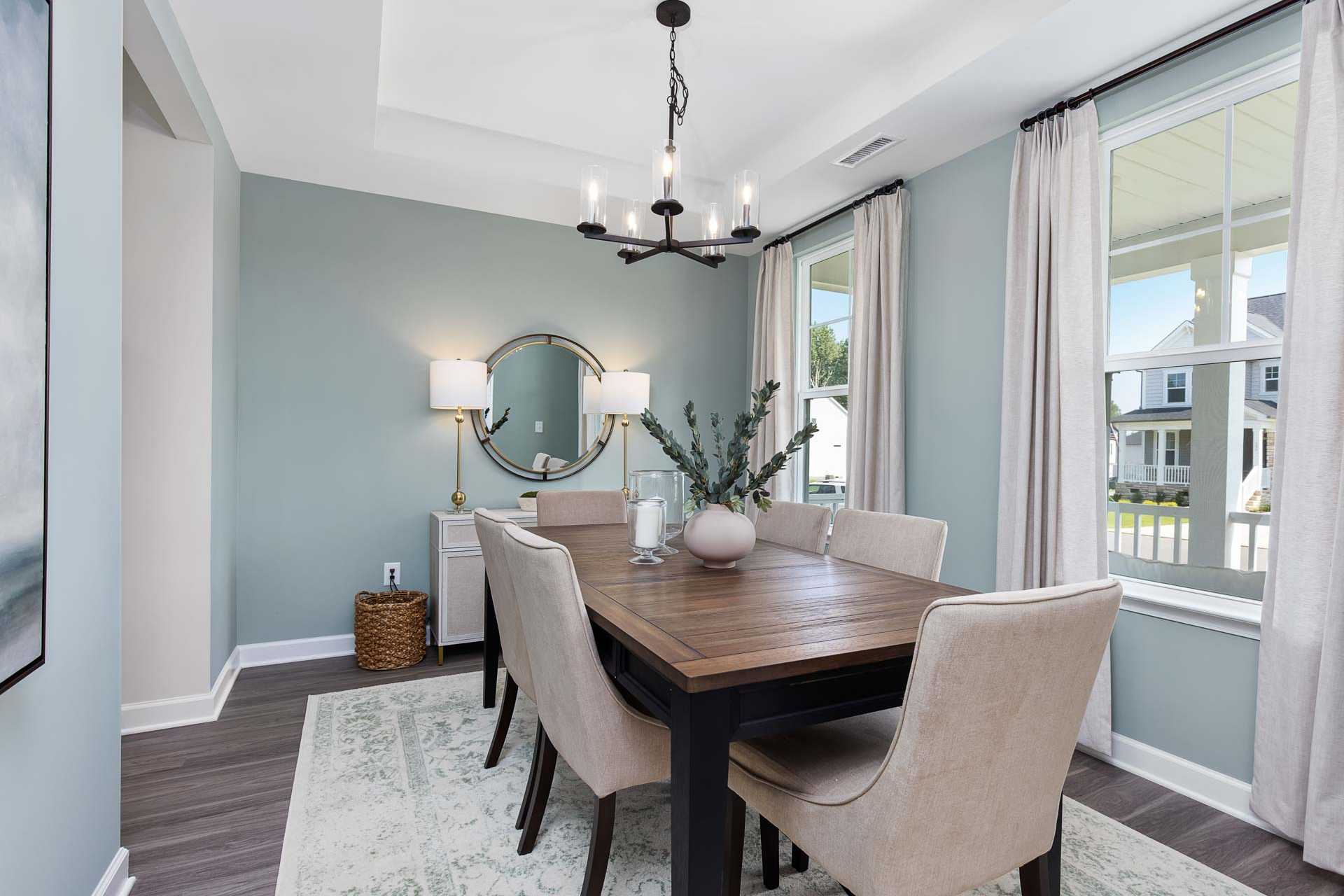 Spacious dining room at Sierra Heights in Clayton NC with wooden farmhouse table, beige upholstered chairs, chandelier, and blue walls