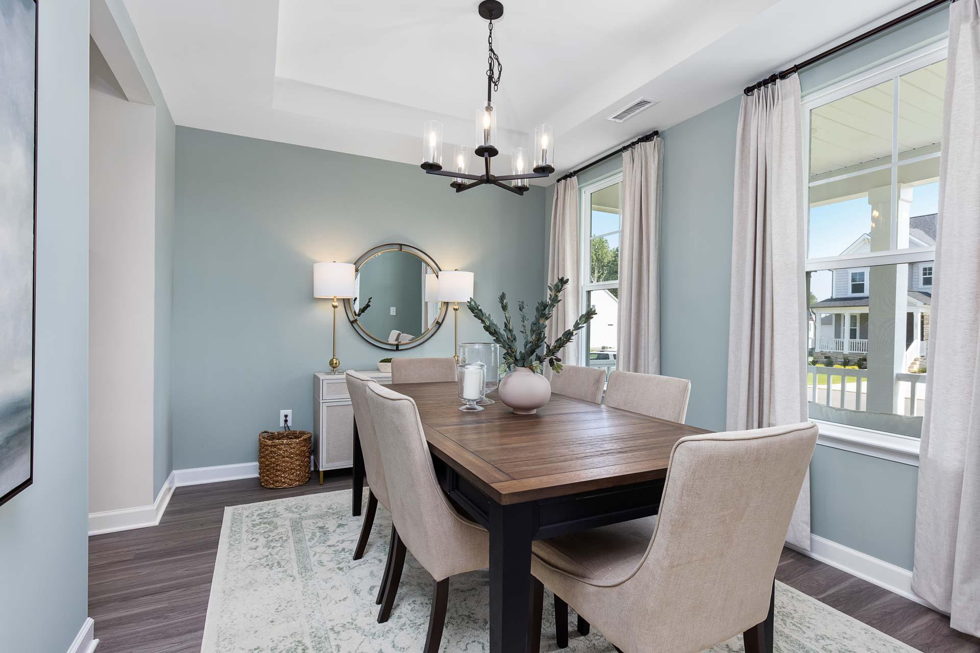 Elegant dining room at Prince Place in Fuquay-Varina, NC with wooden farmhouse table, beige chairs, chandelier, round mirror, and light blue walls