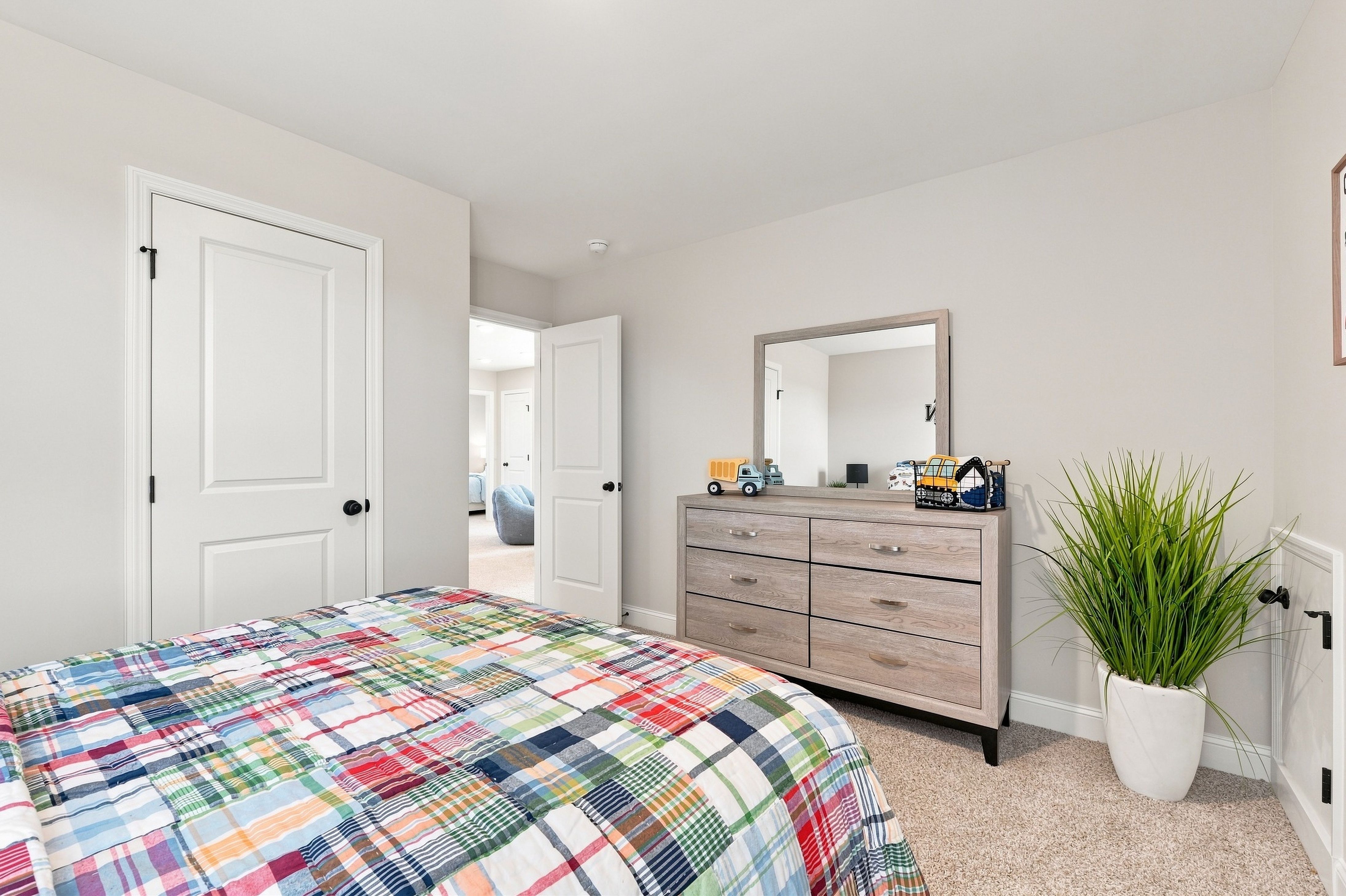Bright bedroom with plaid bedding, wooden dresser, and mirror at Bailey Park by Davidson Homes in Fayetteville, TN