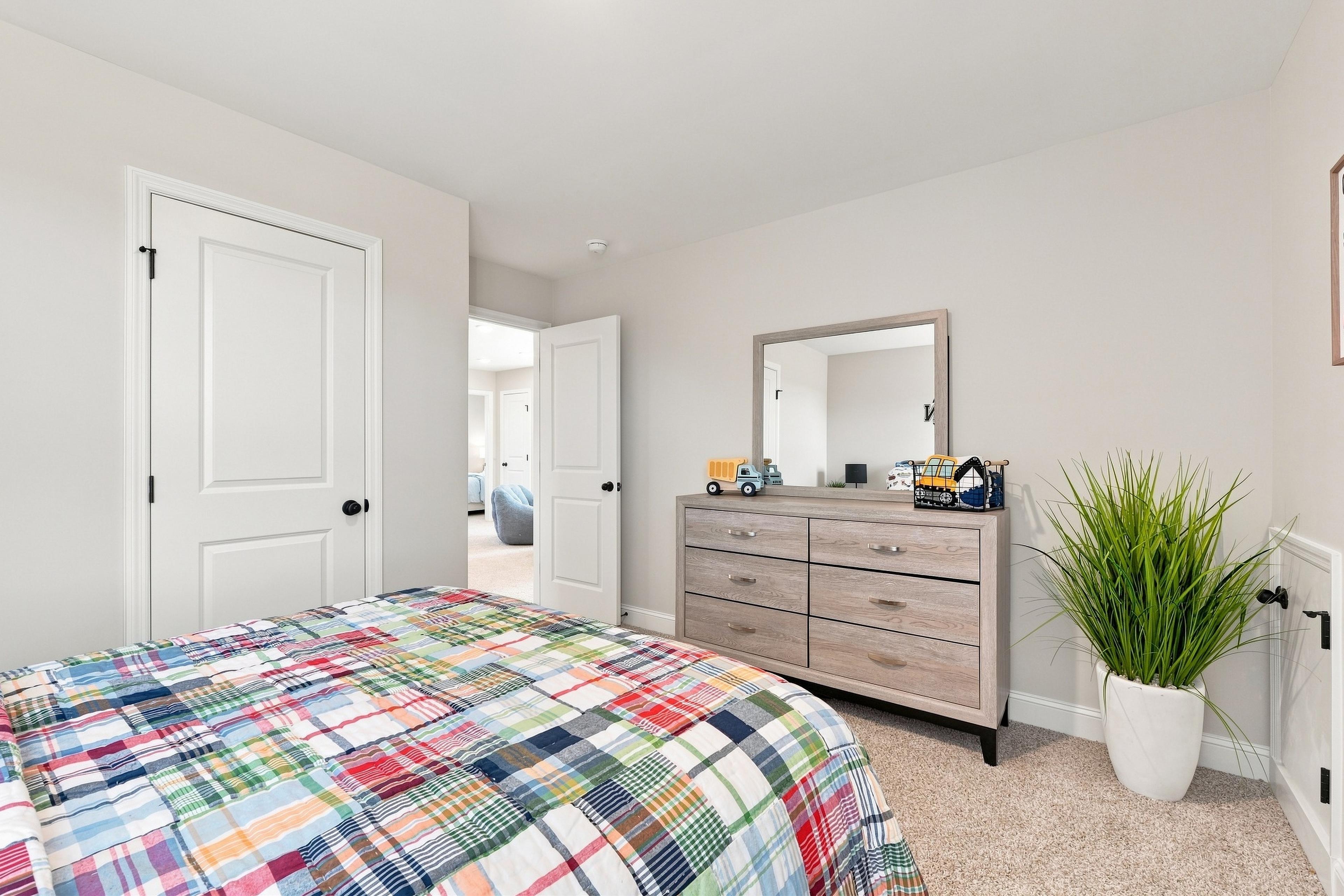 Bright bedroom with plaid bedding, wooden dresser, and mirror at Bailey Park by Davidson Homes in Fayetteville, TN