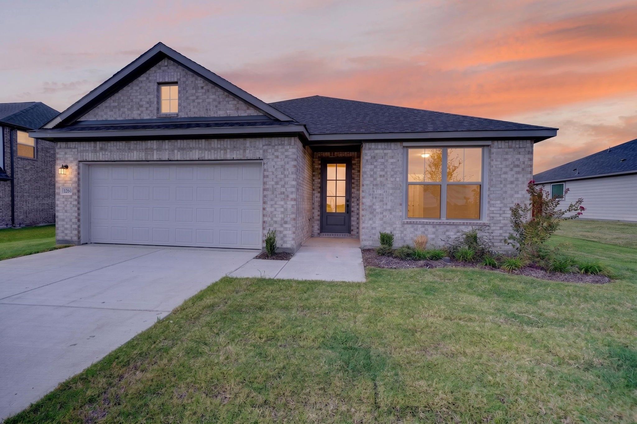 Single-story brick exterior with 2-car garage at dusk in Davidson Homes' The Holly F, Meadow Ridge Estates, Josephine, Texas