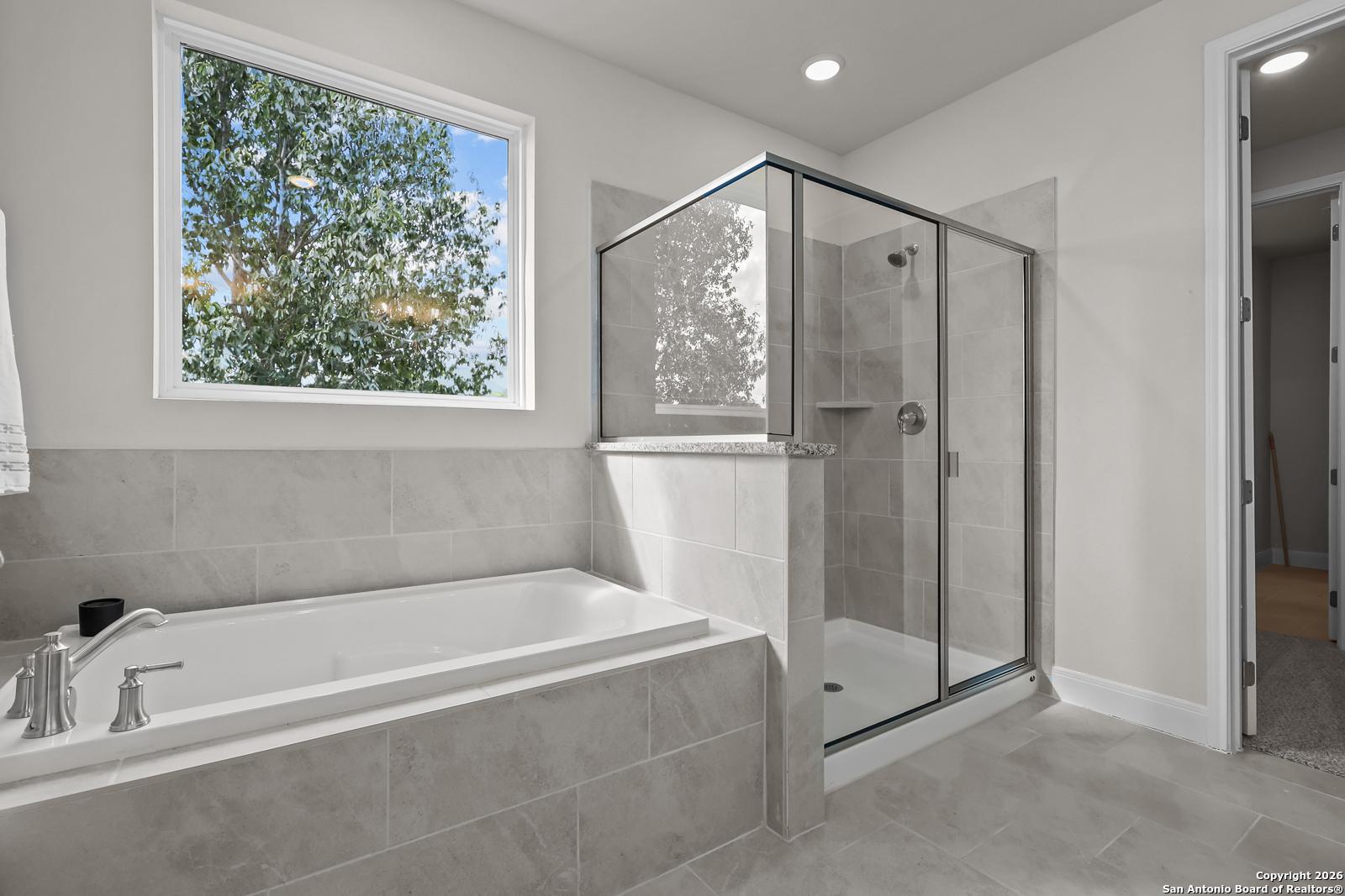Modern master bathroom with freestanding tub, glass shower enclosure, and tree-view window in The Lanier H, Ladera, San Antonio