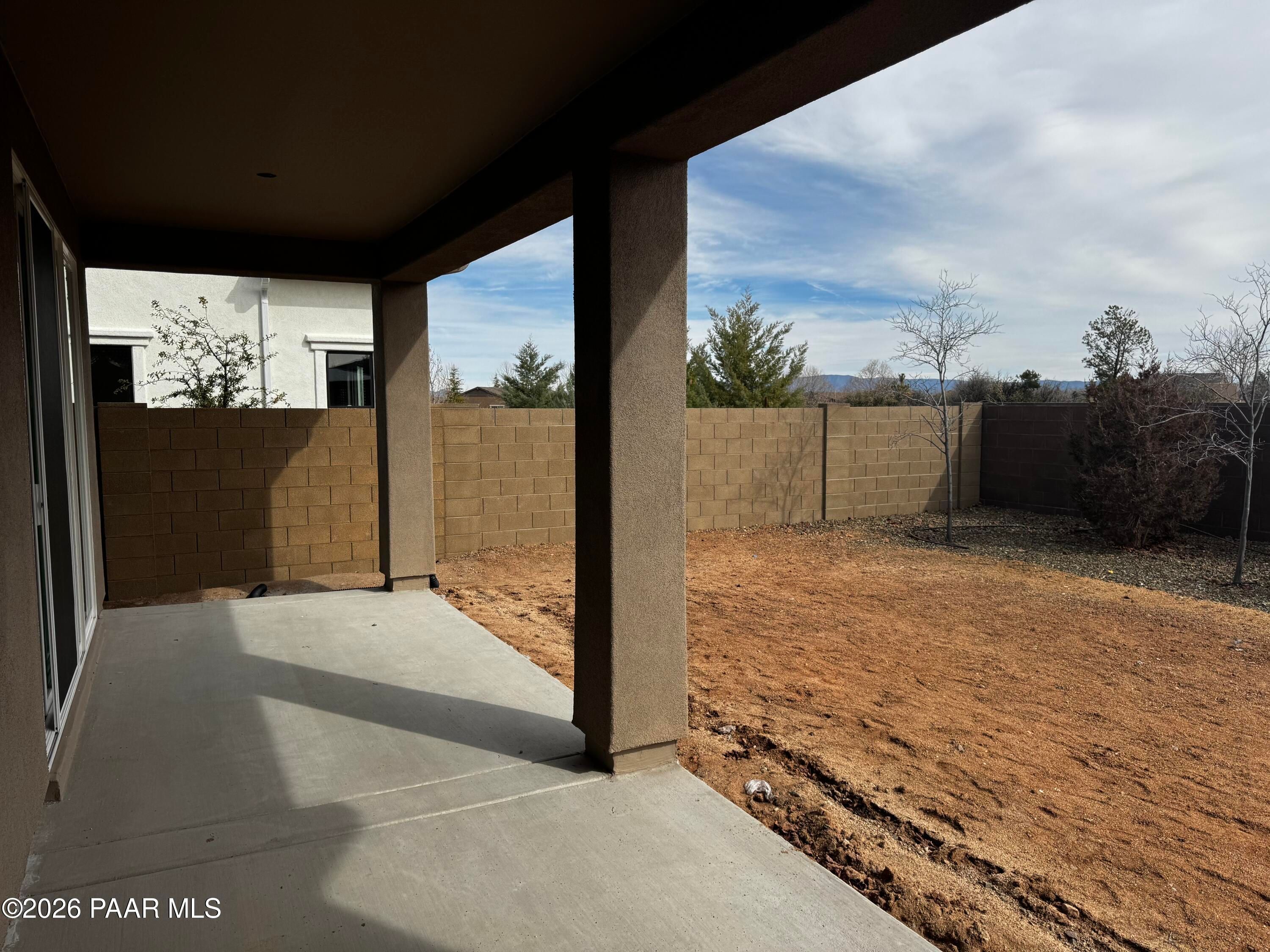 Covered patio with sliding doors, stucco posts, and block fence overlooking dirt yard in Davidson Homes Durango II B, Prescott, AZ