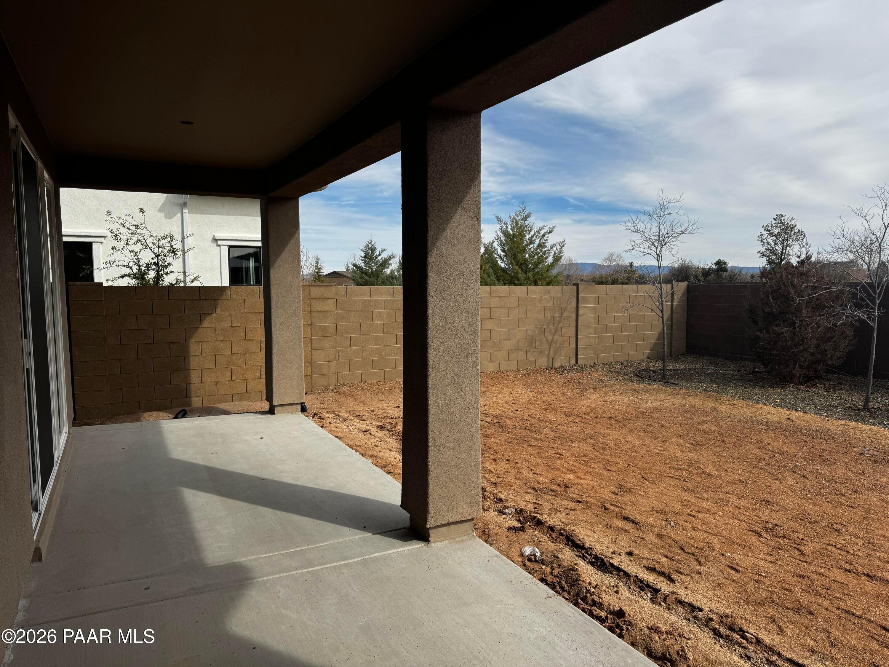 Covered patio with sliding doors, stucco posts, and block fence overlooking dirt yard in Davidson Homes Durango II B, Prescott, AZ