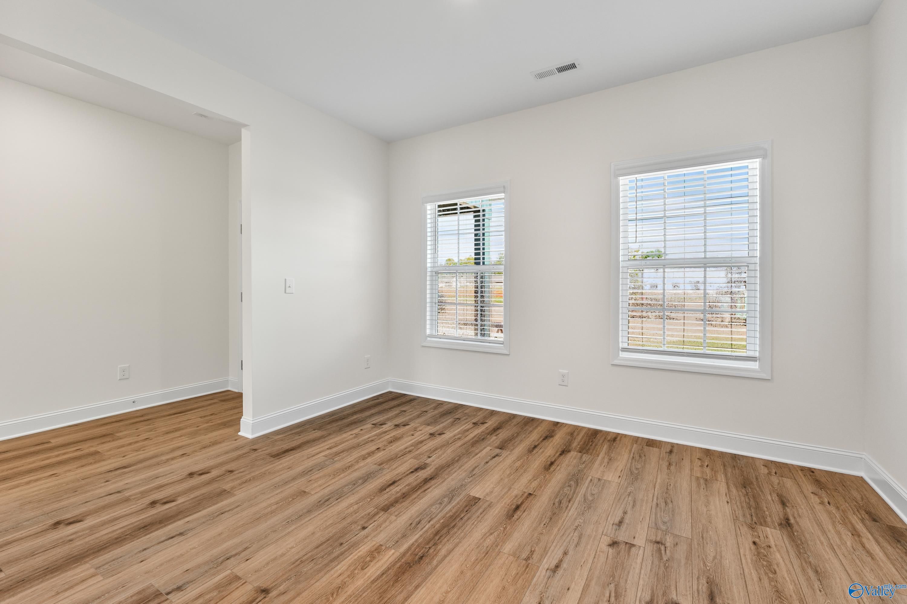 Bright secondary bedroom with light hardwood floors, white walls, and large window blinds in Davidson Homes The Shelby A, Athens, Alabama