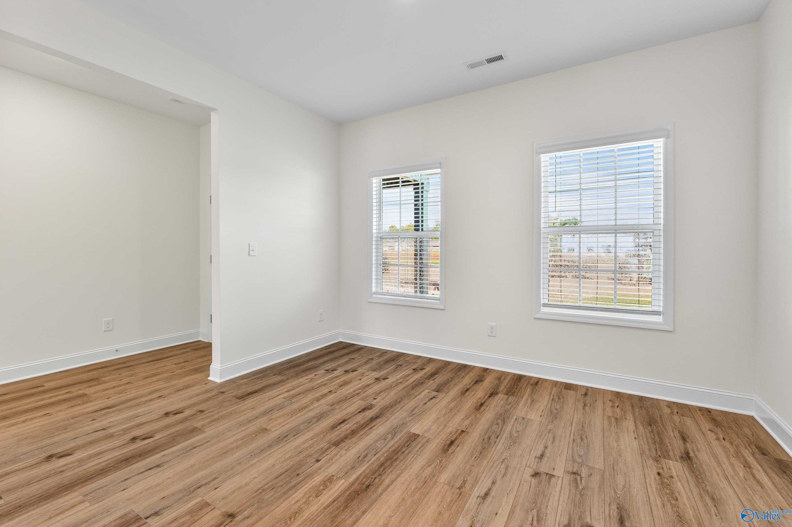 Bright bedroom with light hardwood floors, white walls, and large windows with blinds in Davidson Homes The Shelby A, Athens, Alabama