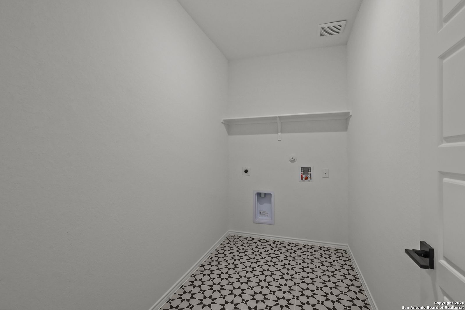 Spacious laundry room with open shelves, washer-dryer hookups, and starburst tile floor in Davidson Homes The Douglas E, San Antonio