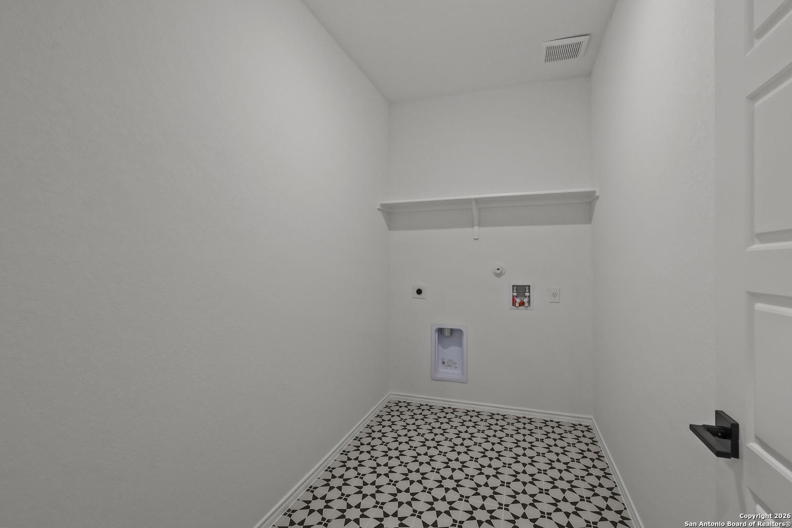 Spacious laundry room with open shelves, washer-dryer hookups, and starburst tile floor in Davidson Homes The Douglas E, San Antonio