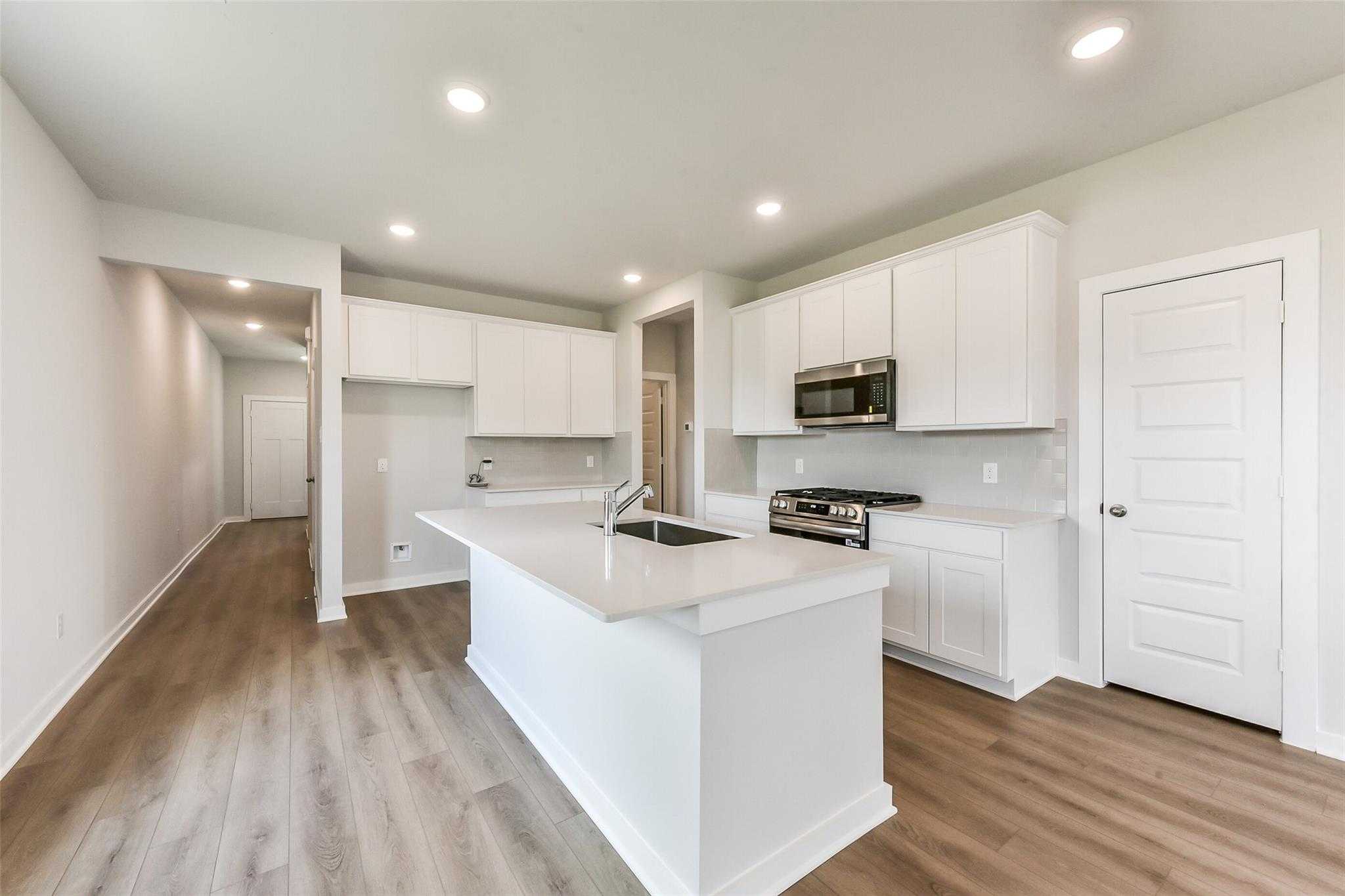 Modern open-concept kitchen with white shaker cabinets, large island sink, stainless appliances in Davidson Homes The Frio F, Dayton Texas