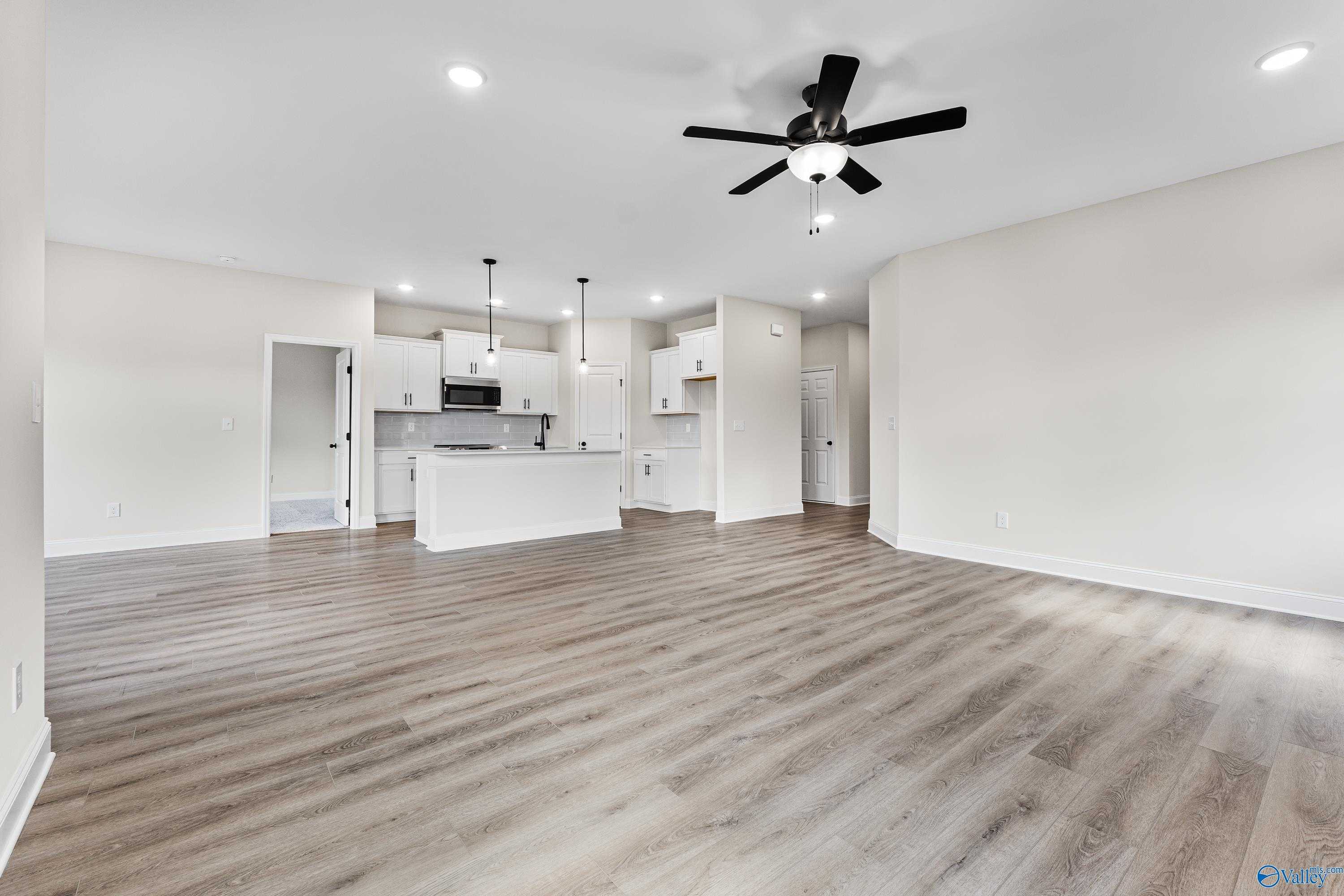 Open-concept kitchen with white cabinets, stainless appliances, and luxury vinyl plank flooring in Davidson Homes Franklin B, Hazel Green, AL