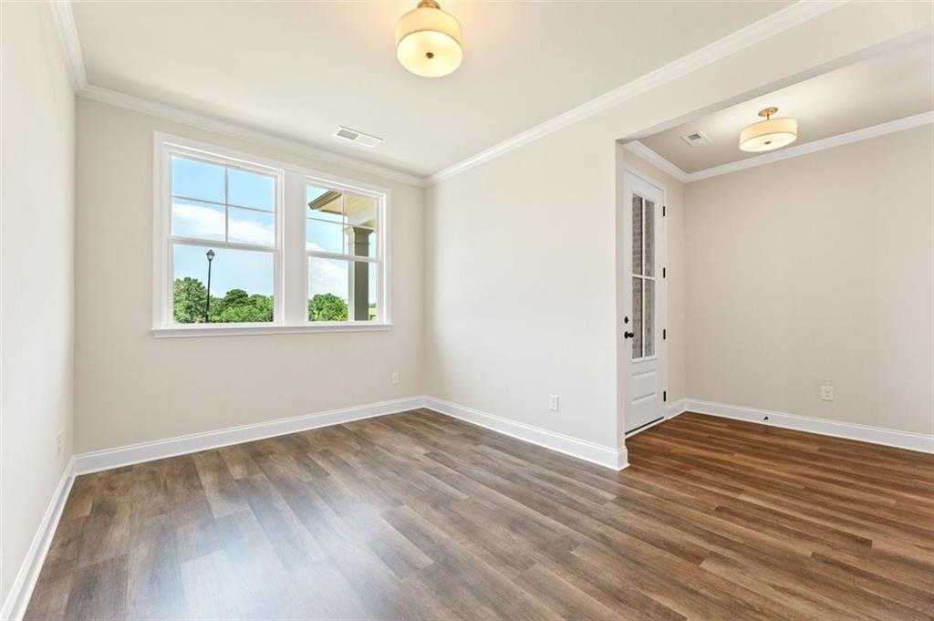 Bright bedroom with hardwood floors, large windows overlooking trees, neutral walls, and ceiling lights in Davidson Homes The Harrison G, Hoschton, GA