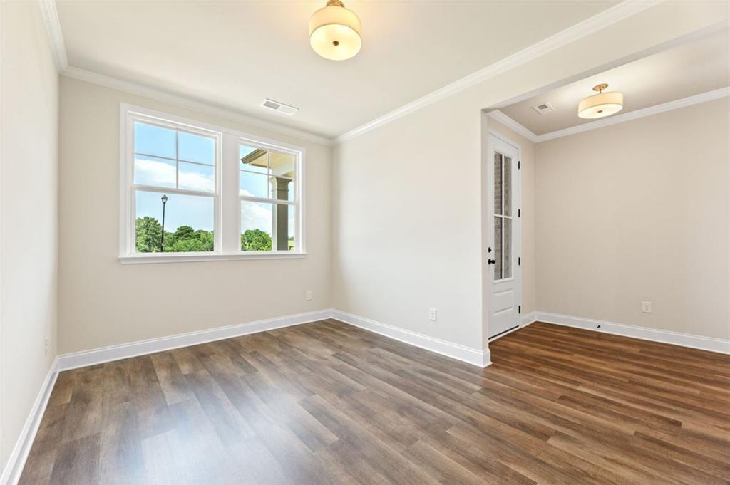 Bright bedroom with hardwood floors, large windows overlooking trees, and arched doorway in Davidson Homes The Harrison G, Hoschton, GA