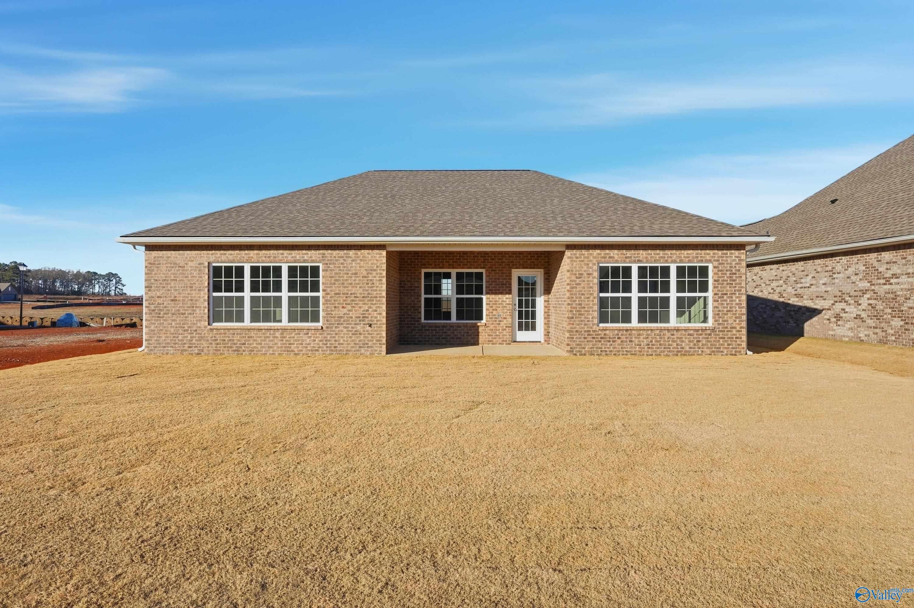 Rear view of brick single-story home with covered entry, large windows, and open yard in Kendall Downs, Toney, Alabama