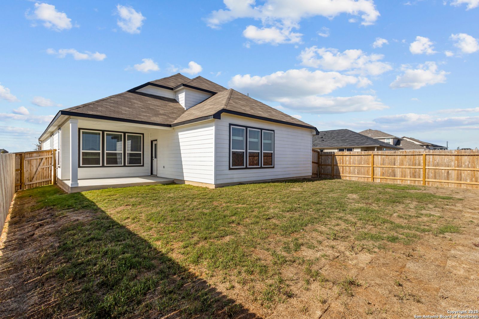 Modern one-story The Collin B home exterior with white siding, covered patio, large windows, and fenced grassy backyard in Hannah Heights, Seguin, Texas