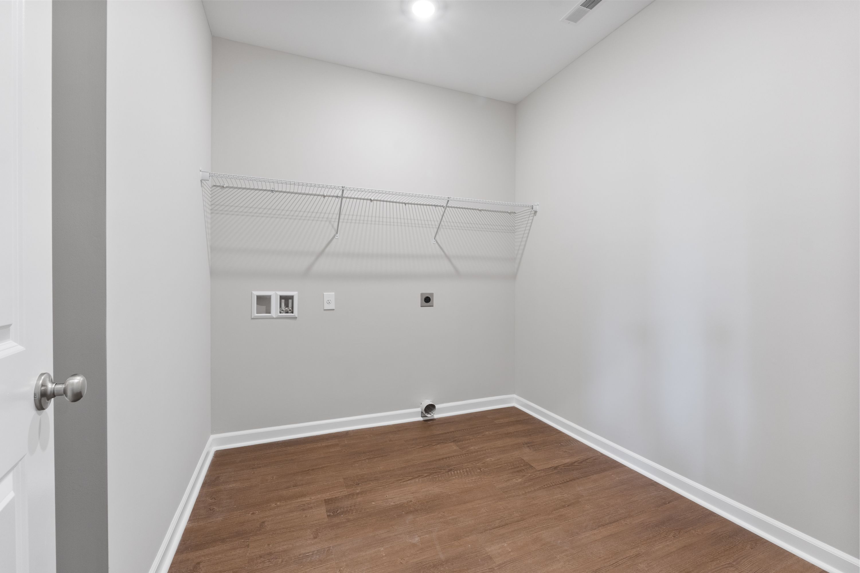 Spacious laundry closet in The Avalon E with hanging rod, shelves, washer-dryer outlets, hardwood floors