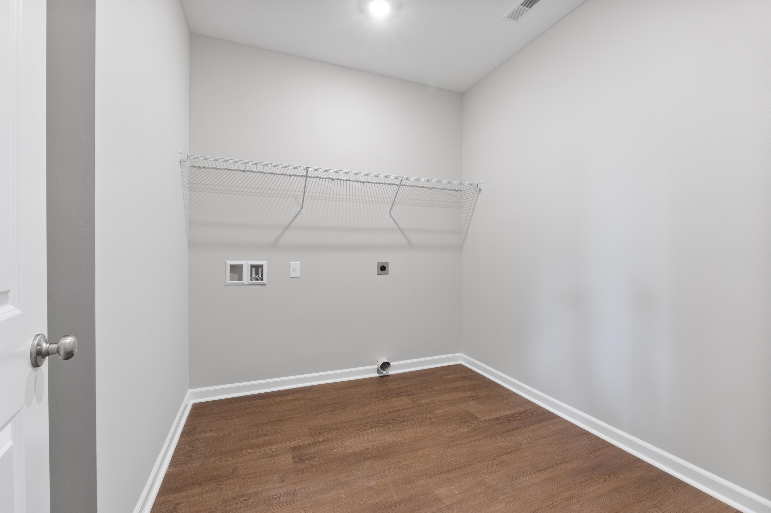Spacious laundry room in The Avalon D by Evermore Homes featuring gray walls, hardwood floors, wire shelving, and washer-dryer hookups