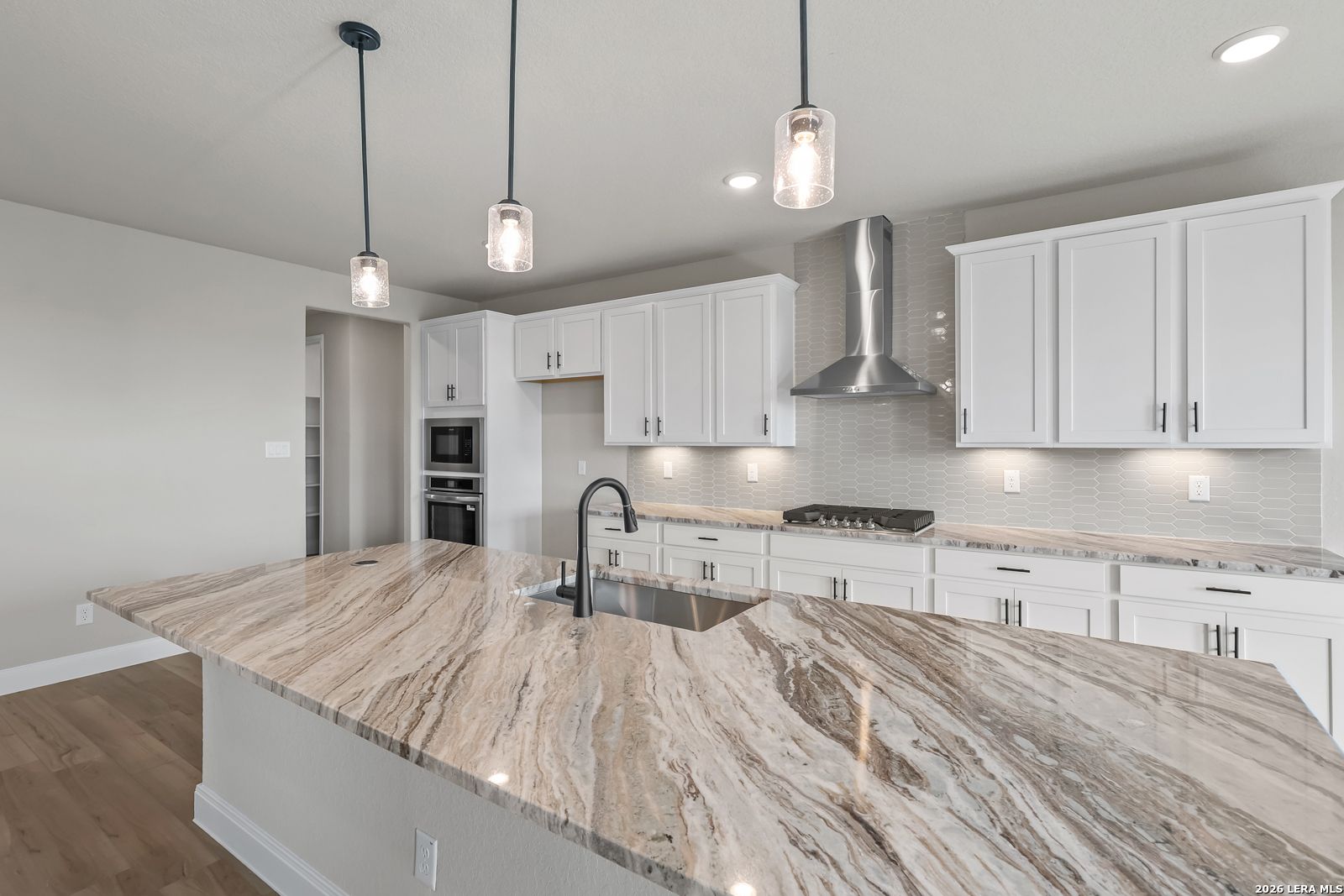 White shaker kitchen with granite island, pendant lights, stainless appliances in Davidson Homes Foster E, Castroville, TX