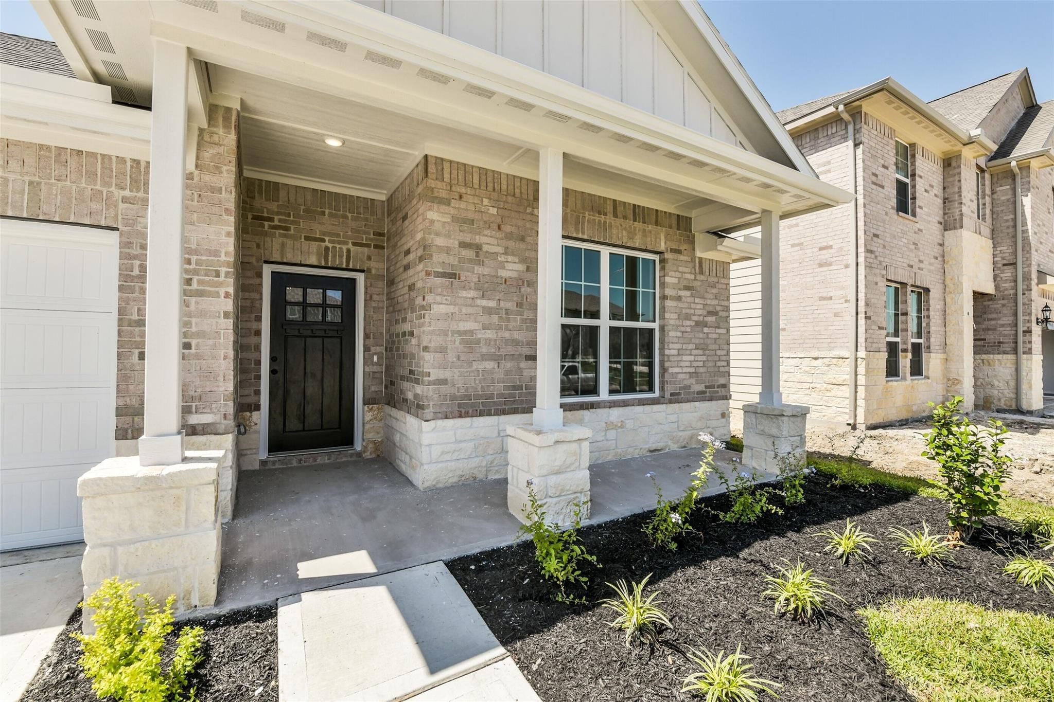 Brick ranch home with covered porch, stone columns, black door, and 2-car garage in Sundance Cove, Crosby, Texas