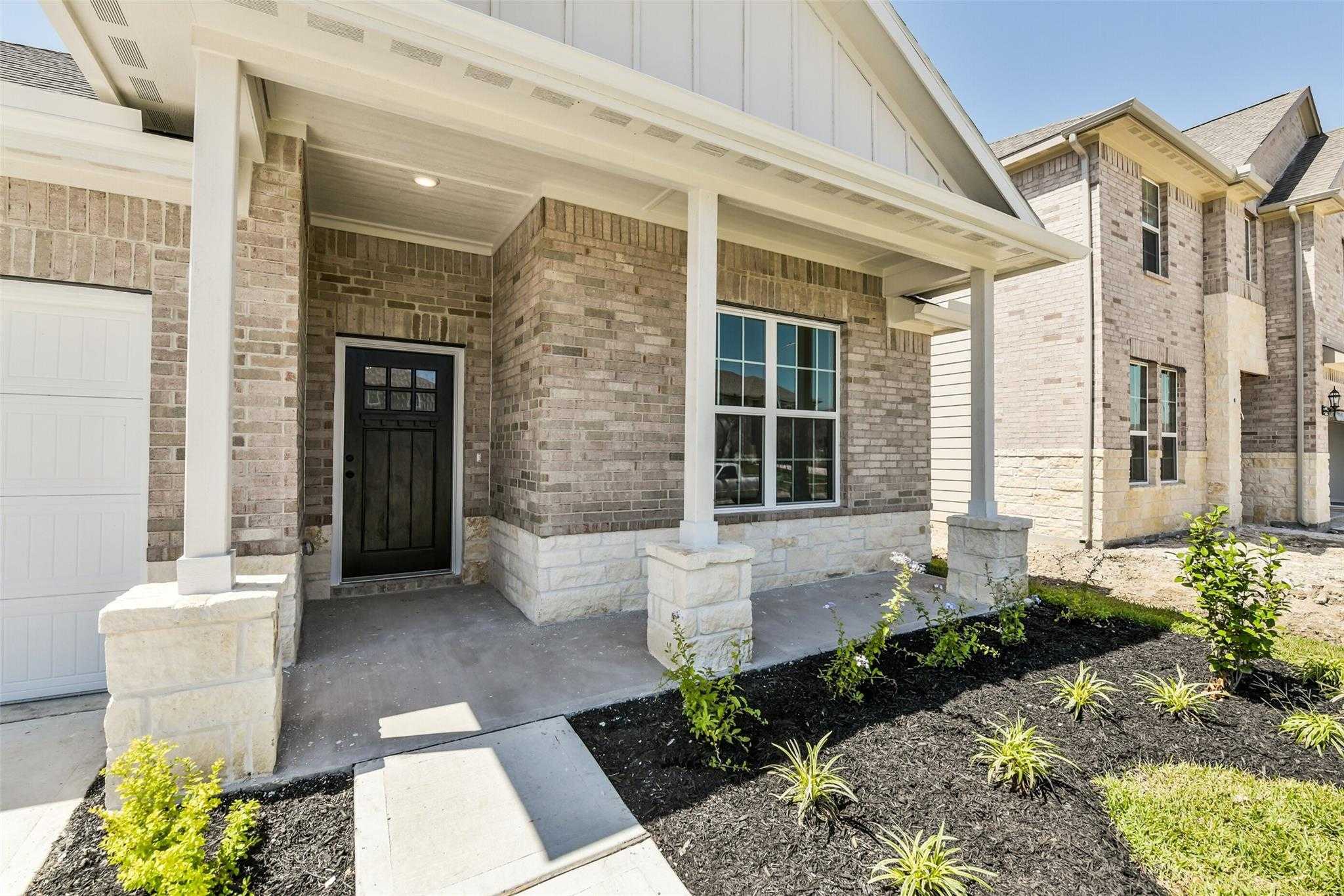 Brick ranch home with covered porch, stone columns, black door, and 2-car garage in Sundance Cove, Crosby, Texas