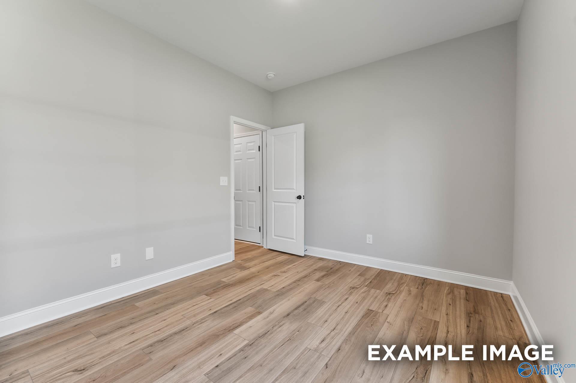 Empty secondary bedroom featuring gray walls, hardwood floors, open white door in The Daphne C 4-bedroom home, Athens, Alabama