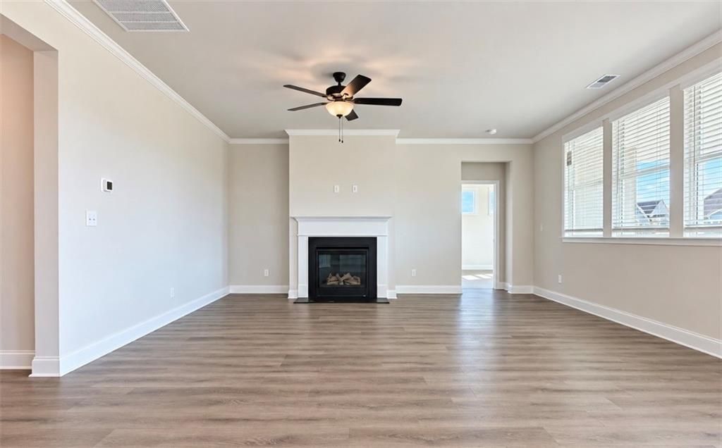 Spacious great room with wood-look flooring, fireplace, and ceiling fan in Davidson Homes The Harrison H, Wehunt Meadows, Hoschton, GA