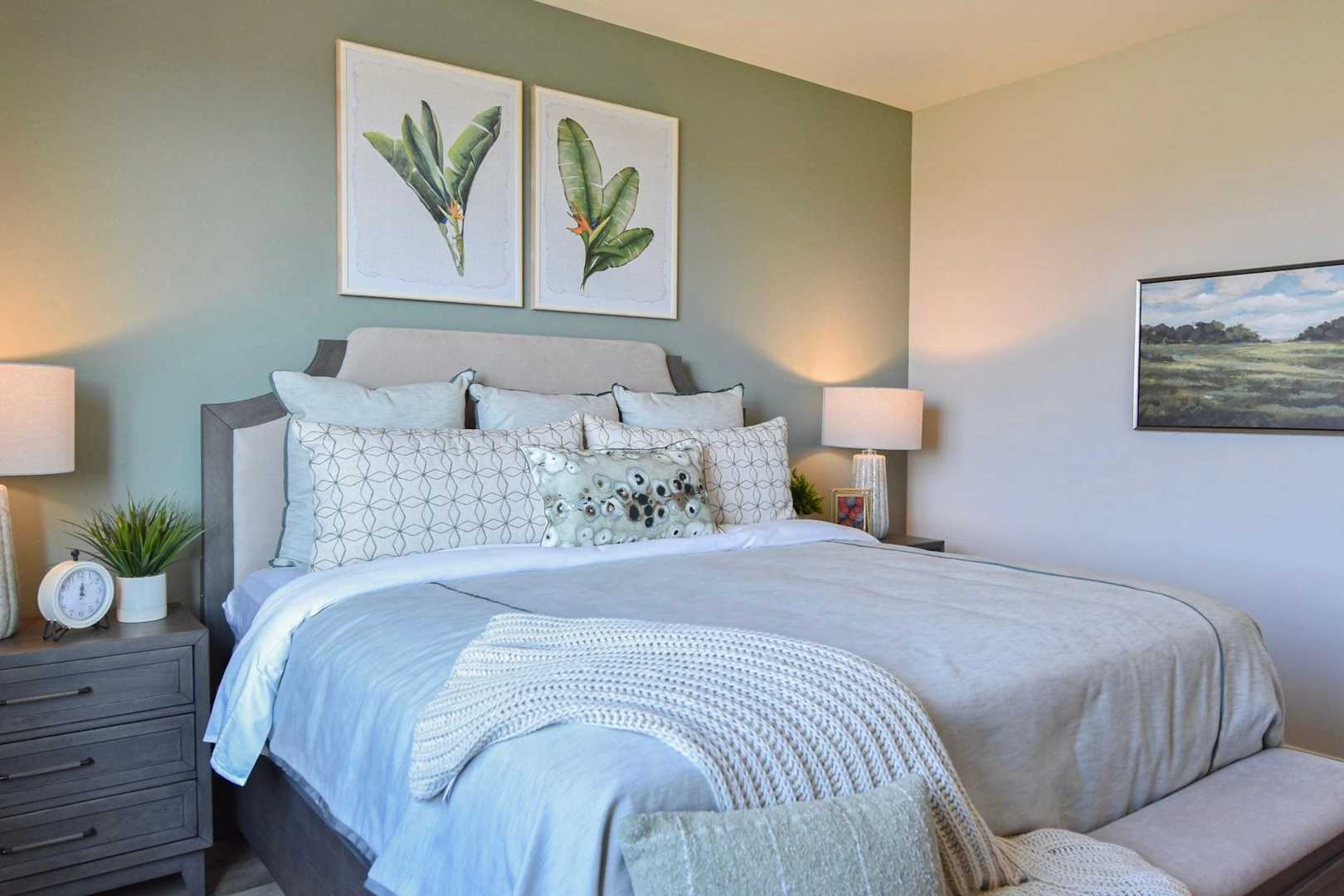 Serene master bedroom in The Harmony with king bed, neutral linens, botanical art, landscape painting, and soft lamps