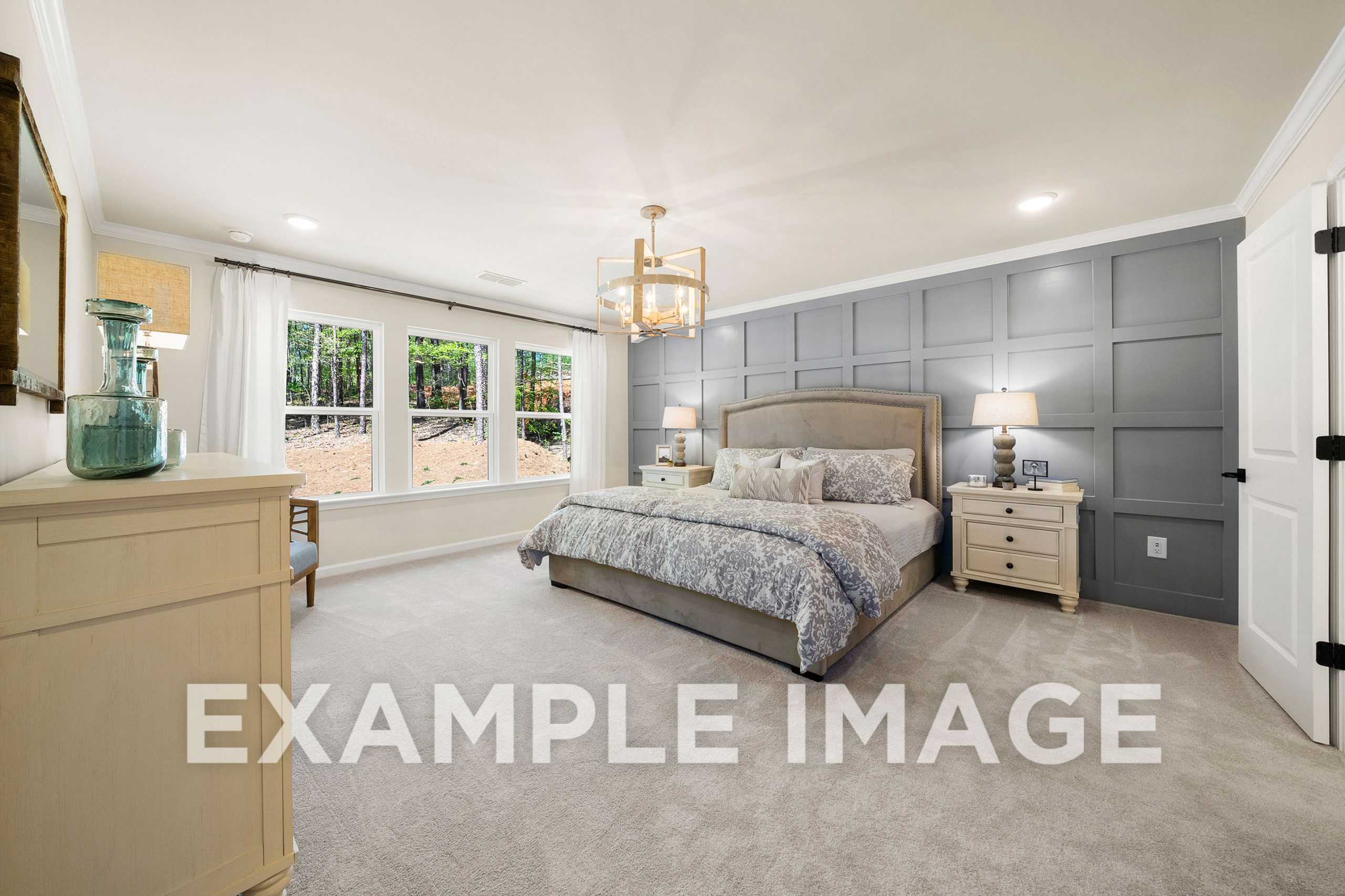 Spacious master bedroom in The Hickory A featuring king bed with patterned duvet, gray shiplap accent wall, chandelier, and large windows
