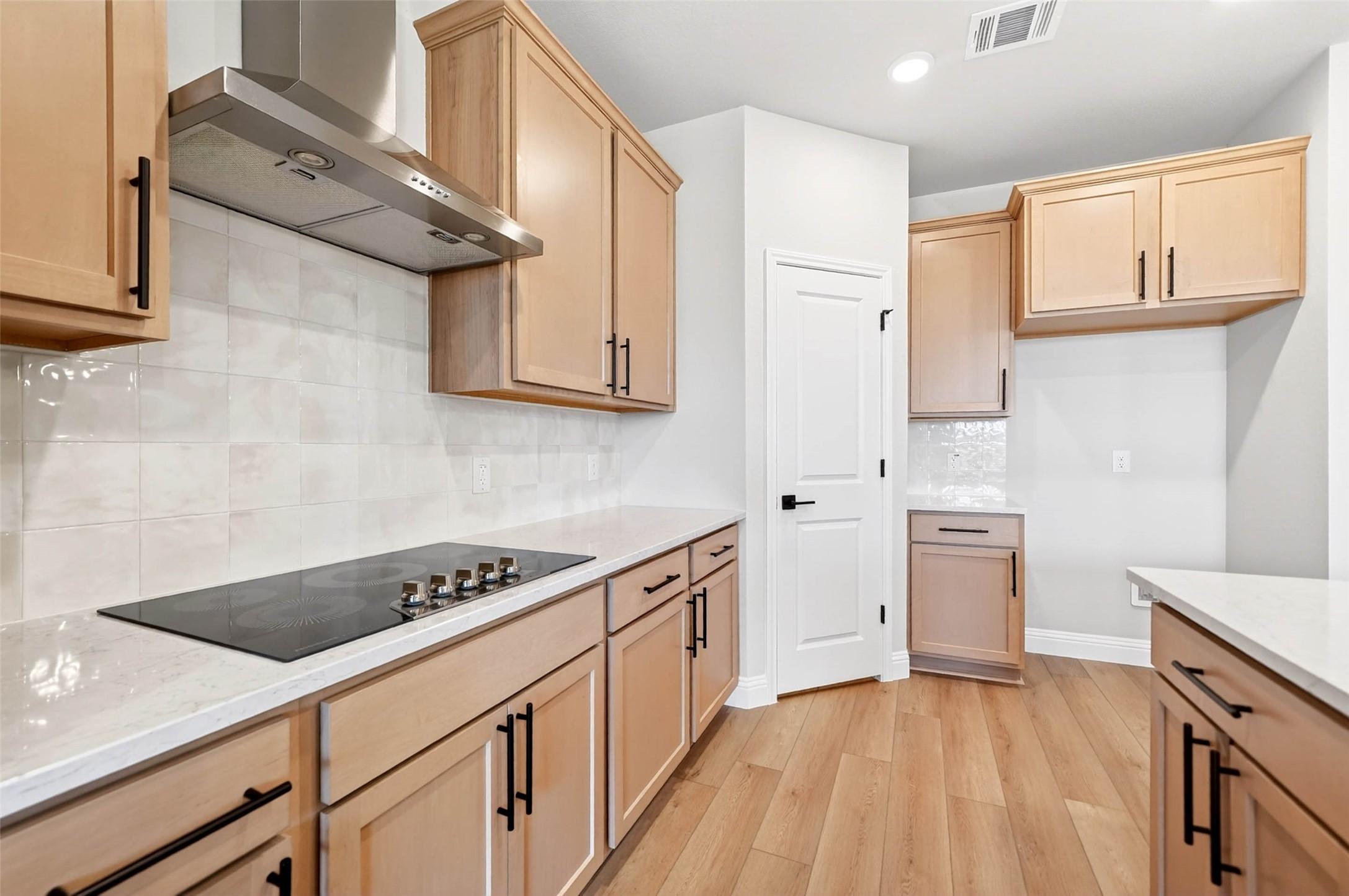 Modern kitchen with light wood cabinets, stone countertops, and stainless vent hood in The Holly C plan, Anna, Texas.