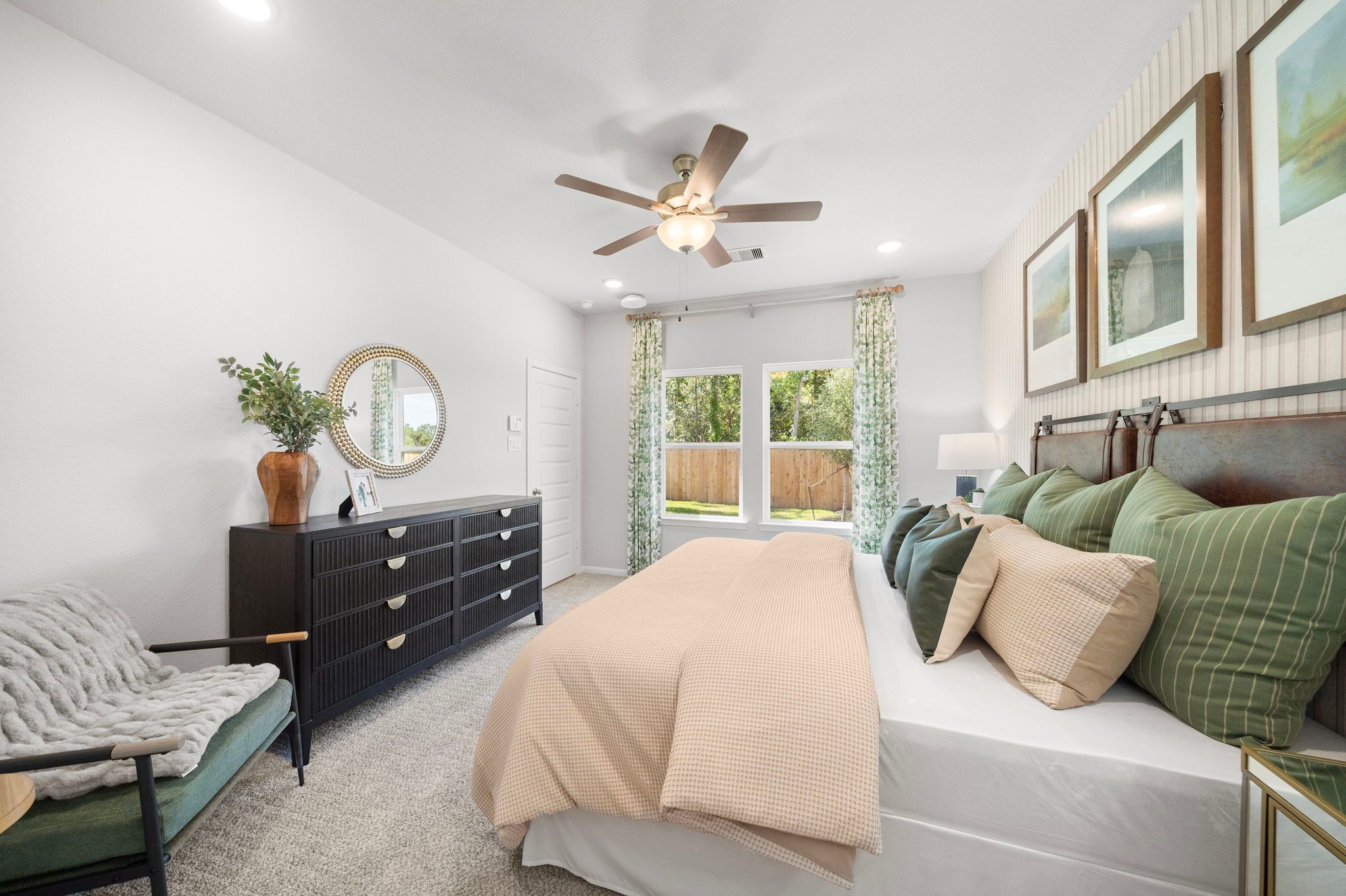 Spacious master bedroom at Robins Landing in Houston Texas with king bed, ceiling fan, black dresser, and garden-view windows