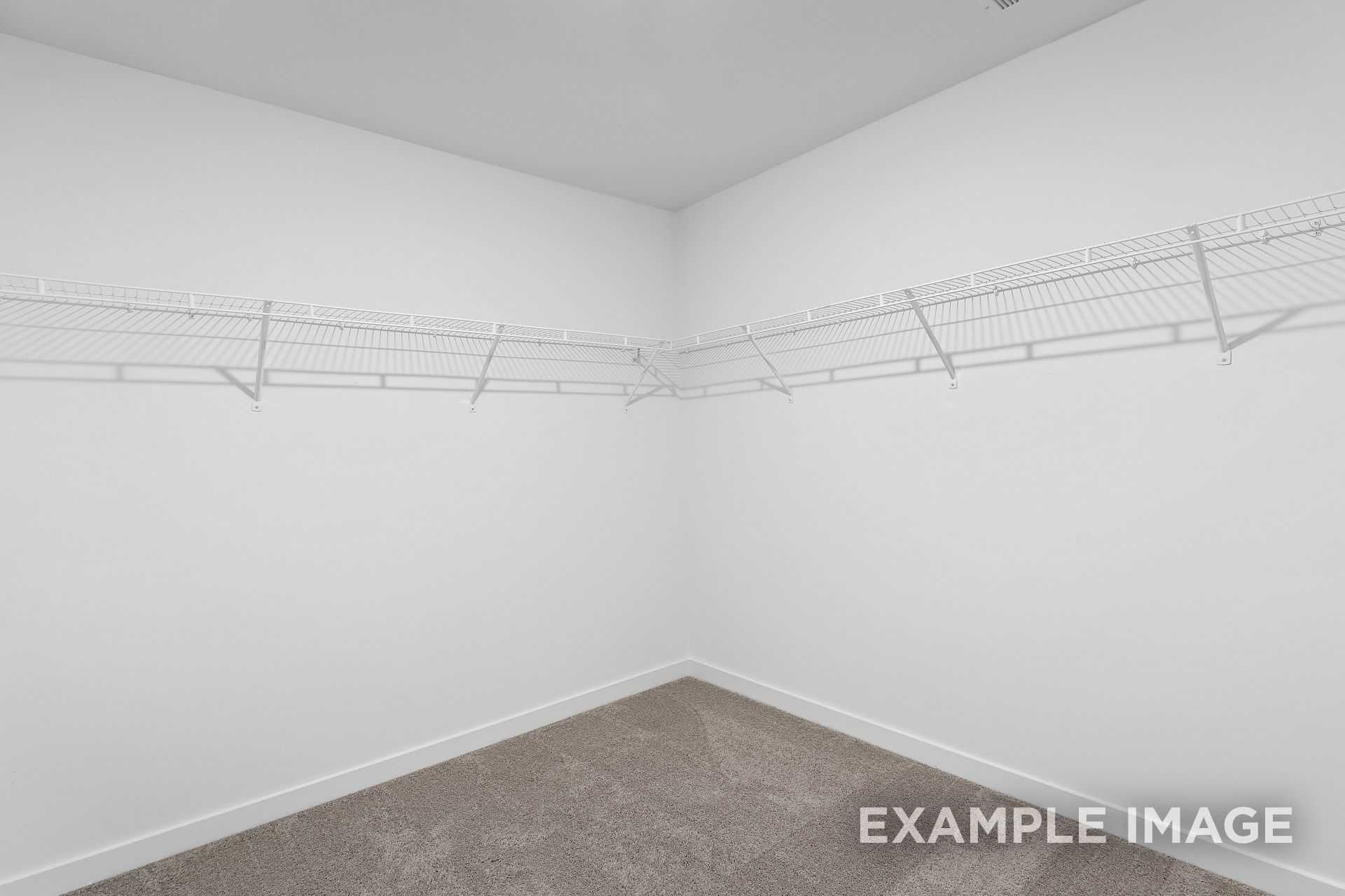 Spacious walk-in closet in The Logan B master suite featuring white wire shelving and neutral carpet flooring