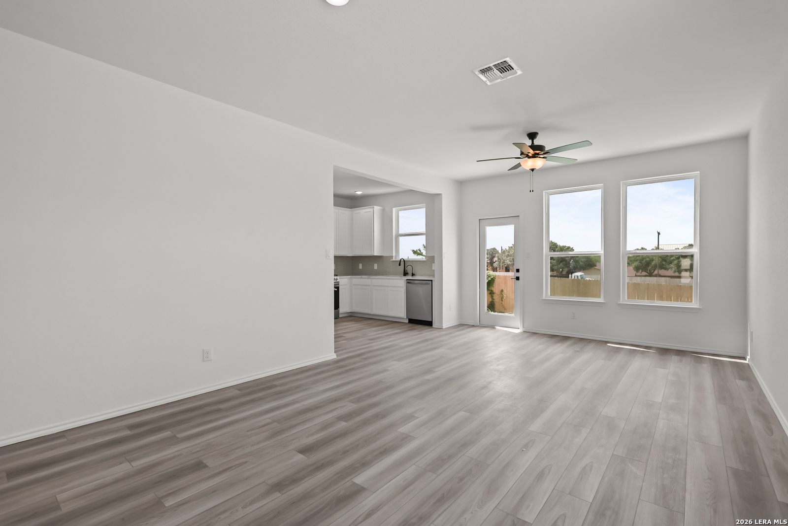Bright open-concept living area with wood-look flooring and kitchen view in The Florence B, Meadows at Oak Creek, San Antonio.