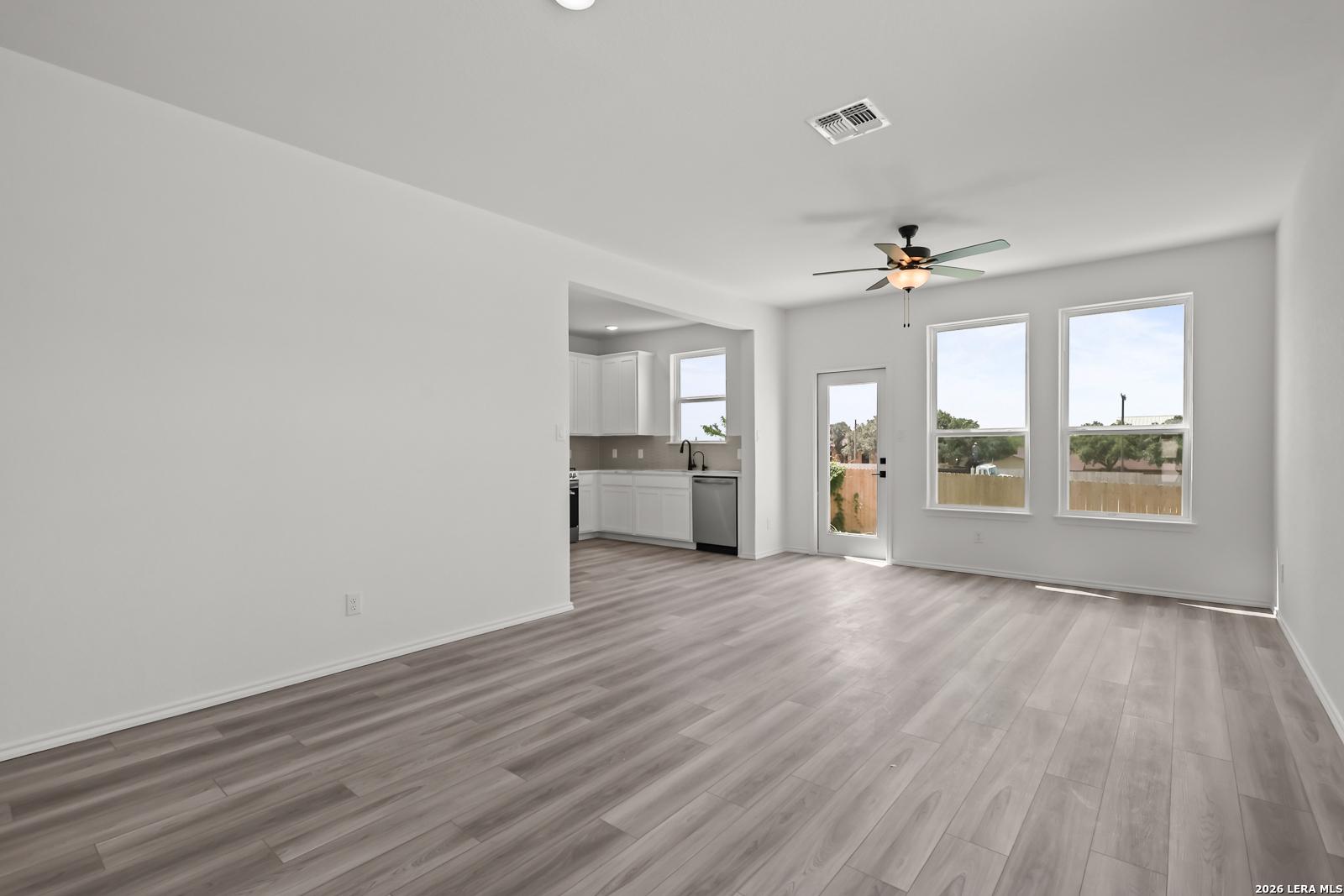 Bright open-concept living area with wood-look flooring and kitchen view in The Florence B, Meadows at Oak Creek, San Antonio.