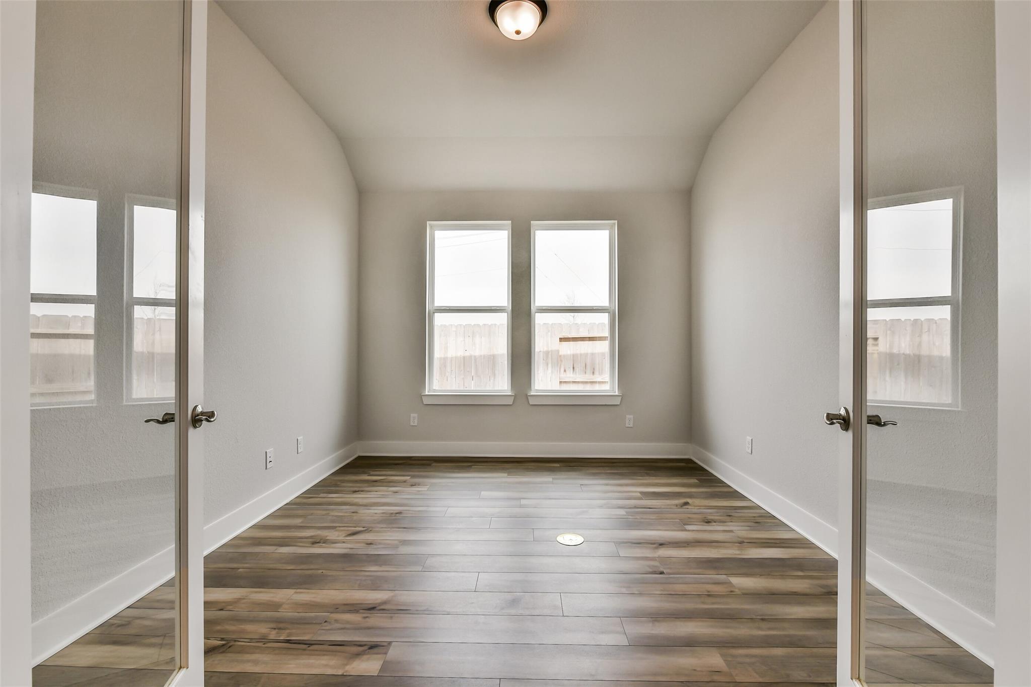 Empty bedroom with hardwood floors, neutral walls, large windows, and French doors in Davidson Homes The George A, Lago Mar, Texas City