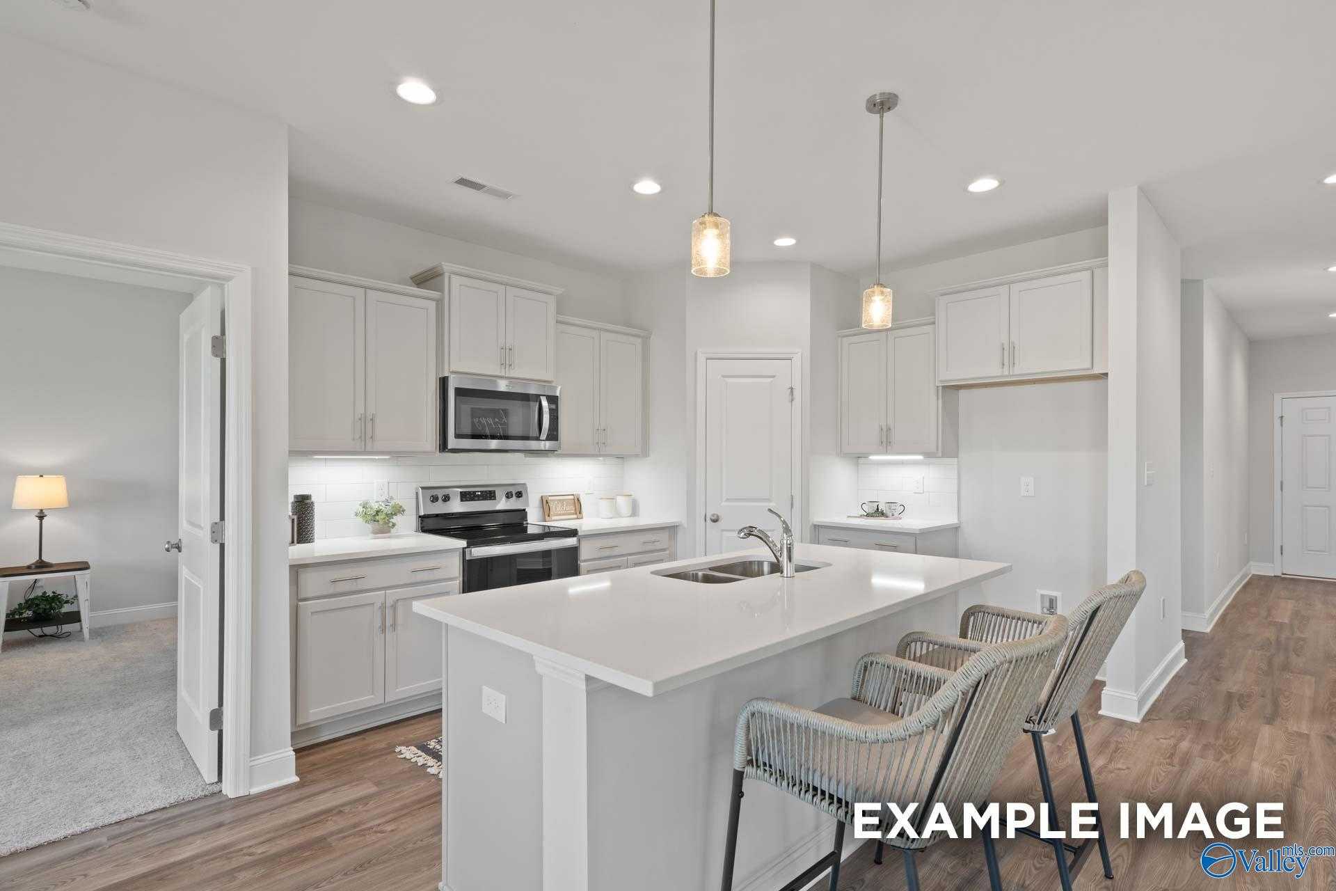 Bright open-concept kitchen with white cabinets, quartz island, bar stools, stainless appliances in Davidson Homes The Franklin C, Meridianville, AL