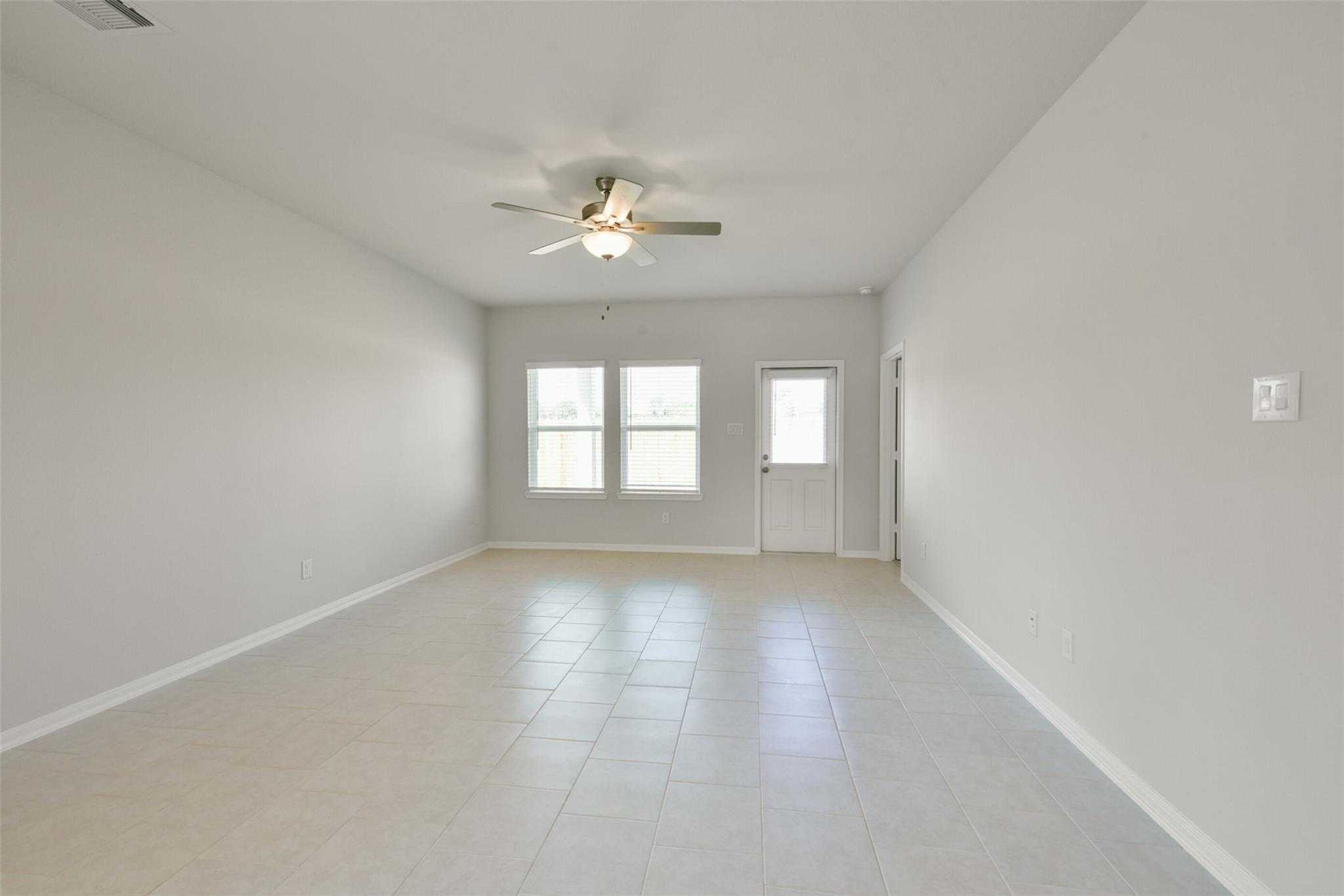 Bright open living room with gray tile floors, ceiling fan, and large windows in Davidson Homes Sabine E, Dayton Texas