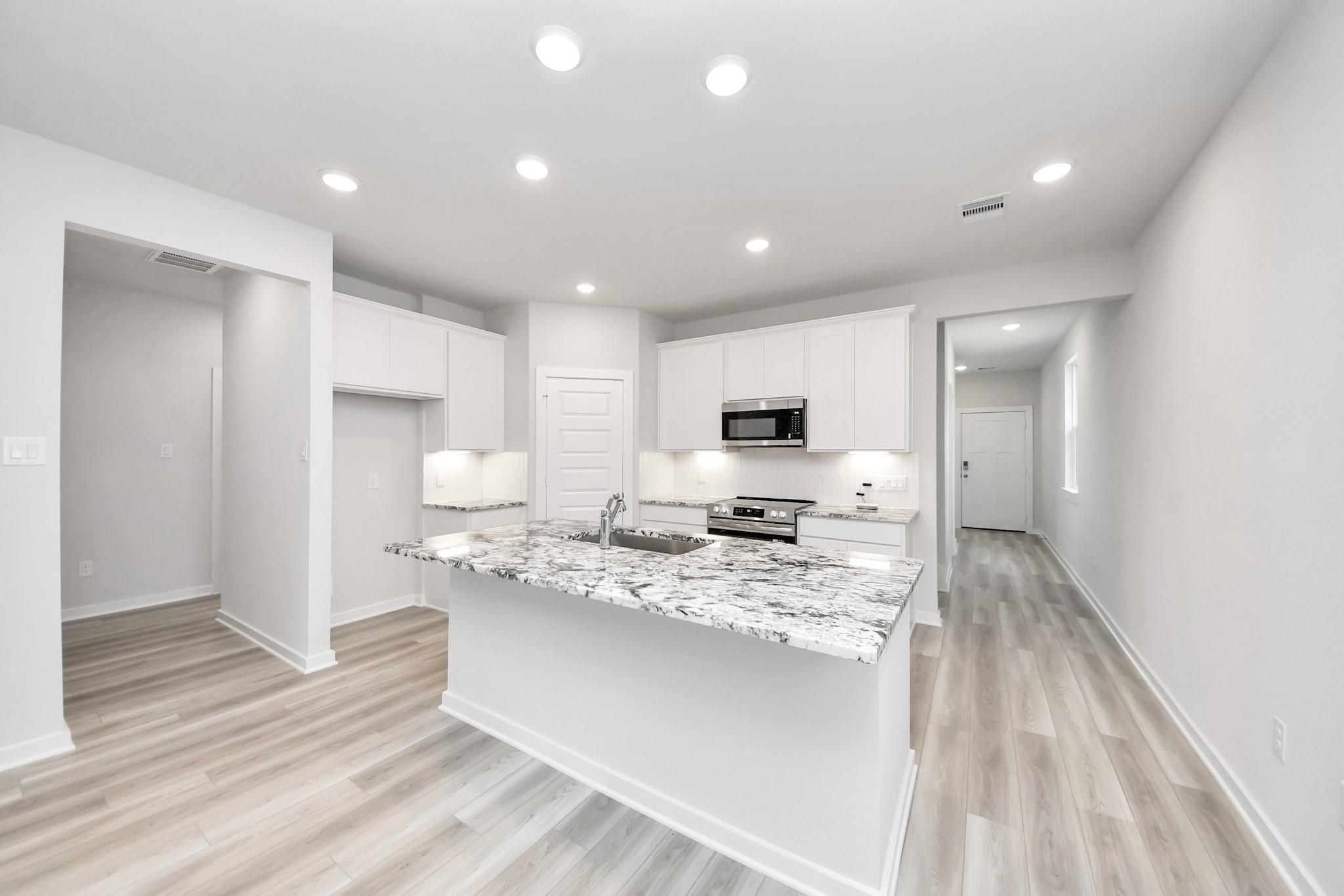 Modern kitchen with granite island and white cabinets in The Sabine F floor plan by Davidson Homes in Cleveland, Texas.