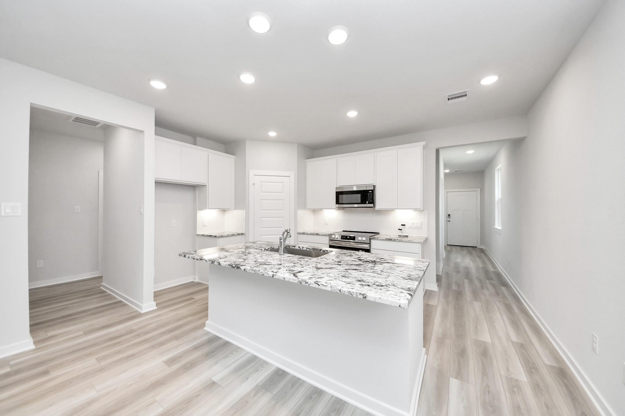Modern kitchen with granite island and white cabinets in The Sabine F floor plan by Davidson Homes in Cleveland, Texas.