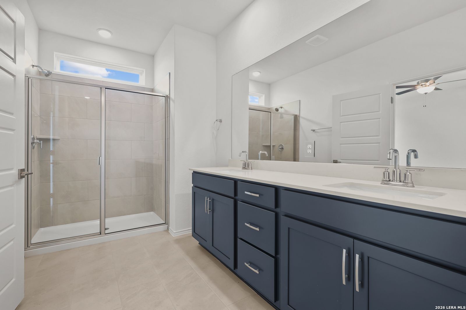 Modern primary bathroom featuring glass-enclosed walk-in shower, navy double vanity with quartz countertop, and clerestory window in Davidson Homes The Glenwood E, Elmendorf Texas