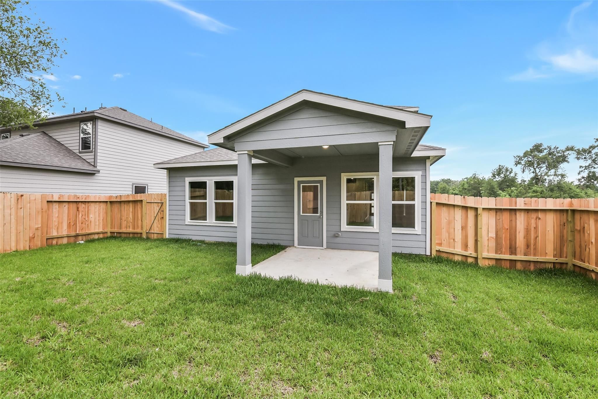Gray two-story home with covered back patio, windows, and fenced grassy yard in Caney Creek Place, Conroe, Texas - Davidson Homes Brazos F