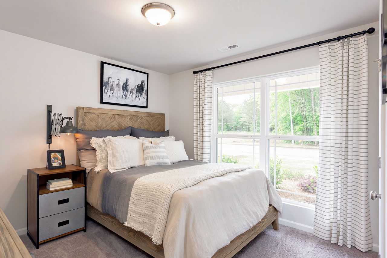 Cozy secondary bedroom in The Franklin home by Davidson Homes featuring queen bed with wooden headboard, large window with sheer curtains, horse wall art
