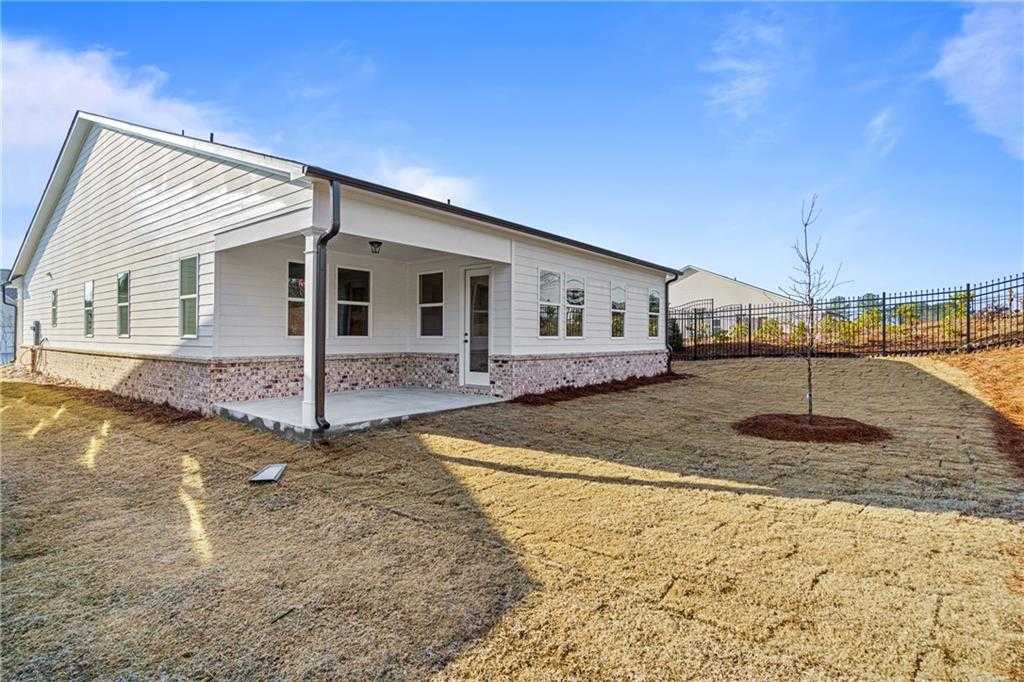 Side view of white single-story The Edison A home with covered porch, brick base, and fenced yard in Kelly Preserve, Loganville, Georgia