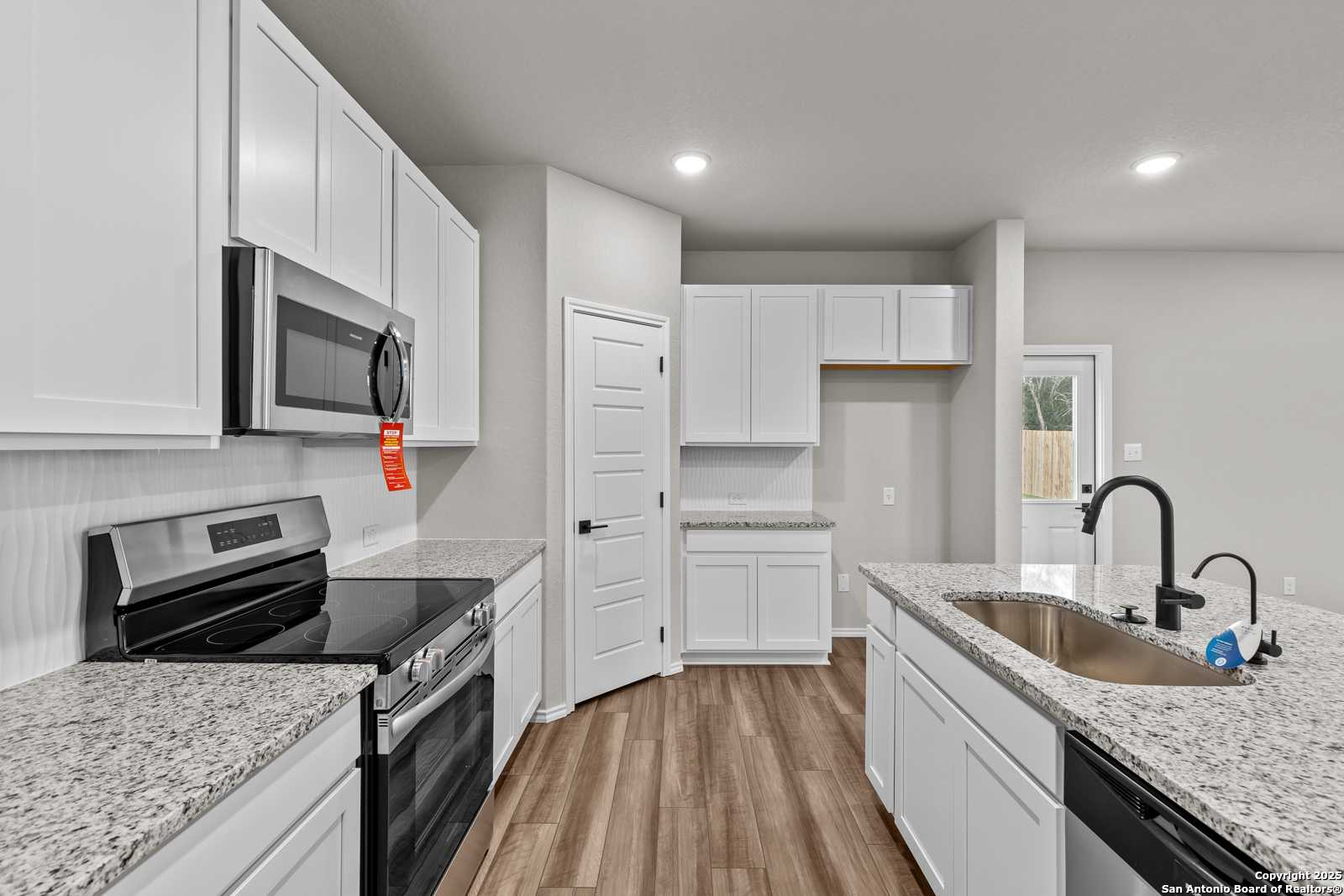 Modern kitchen with white cabinets, granite countertops, stainless appliances in The Murray I by Davidson Homes, San Antonio